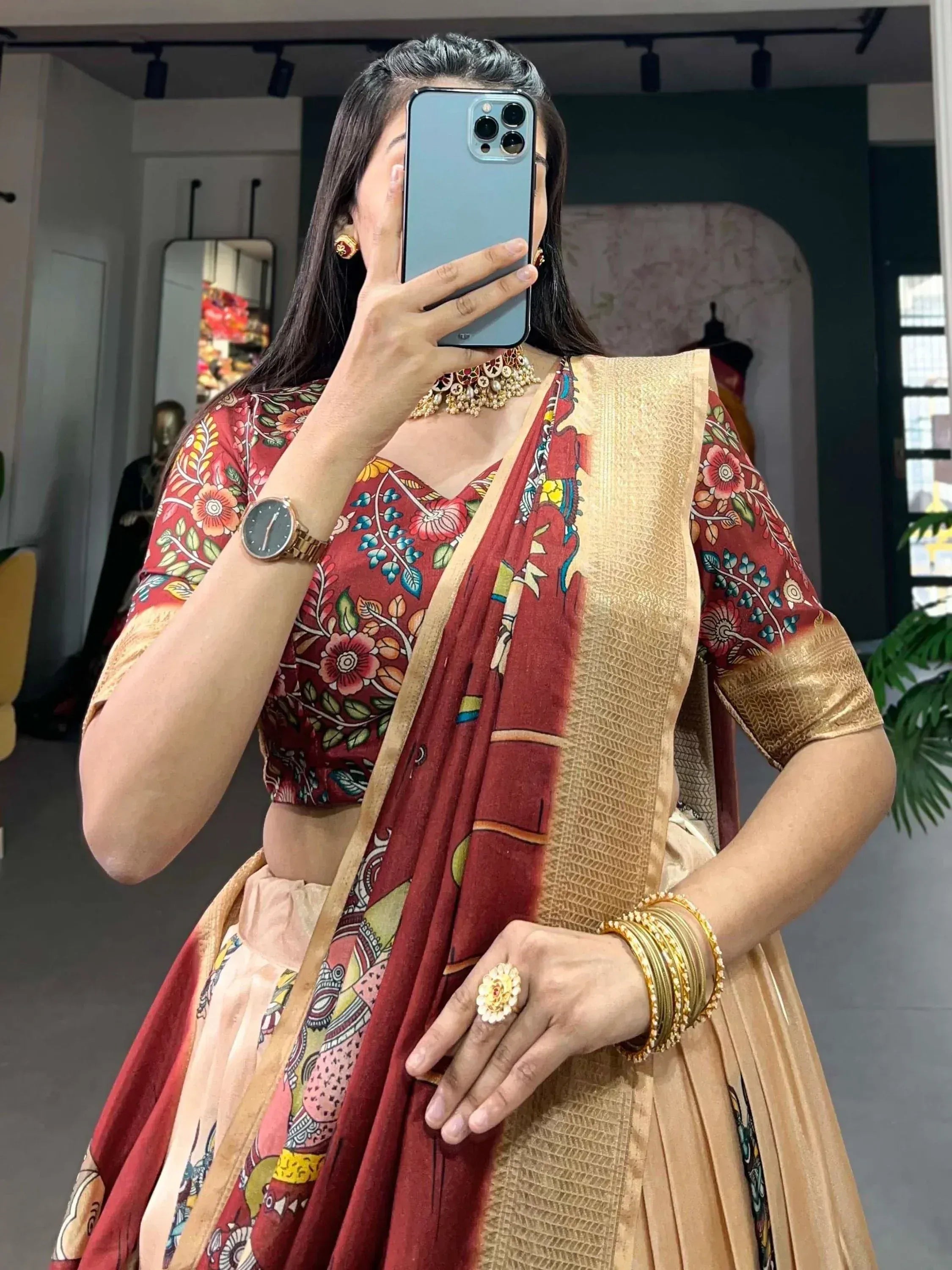 Woman in floral red and gold lehenga choli with traditional jewelry, taking mirror selfie