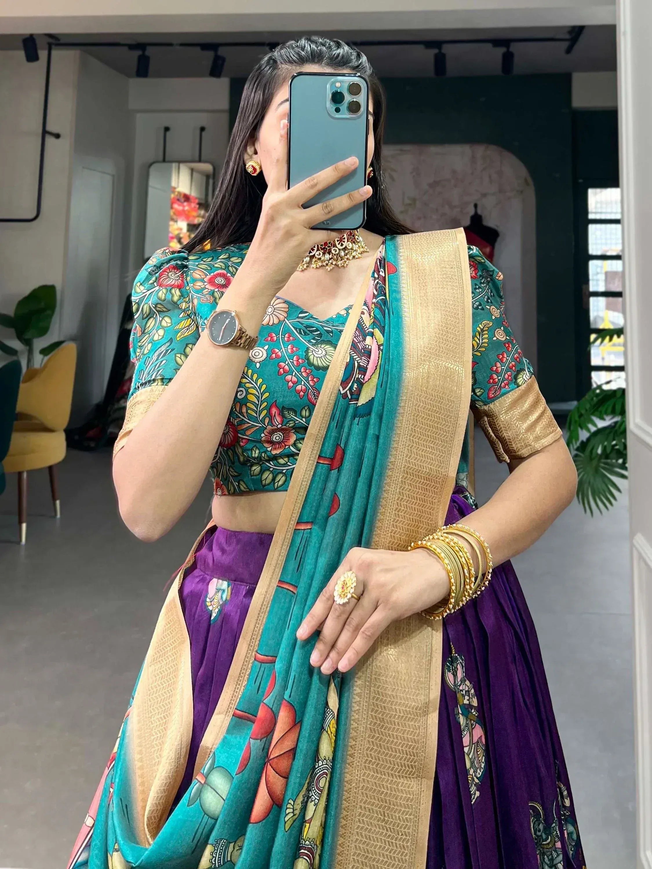 Woman in teal floral blouse and purple lehenga with gold border, taking mirror selfie