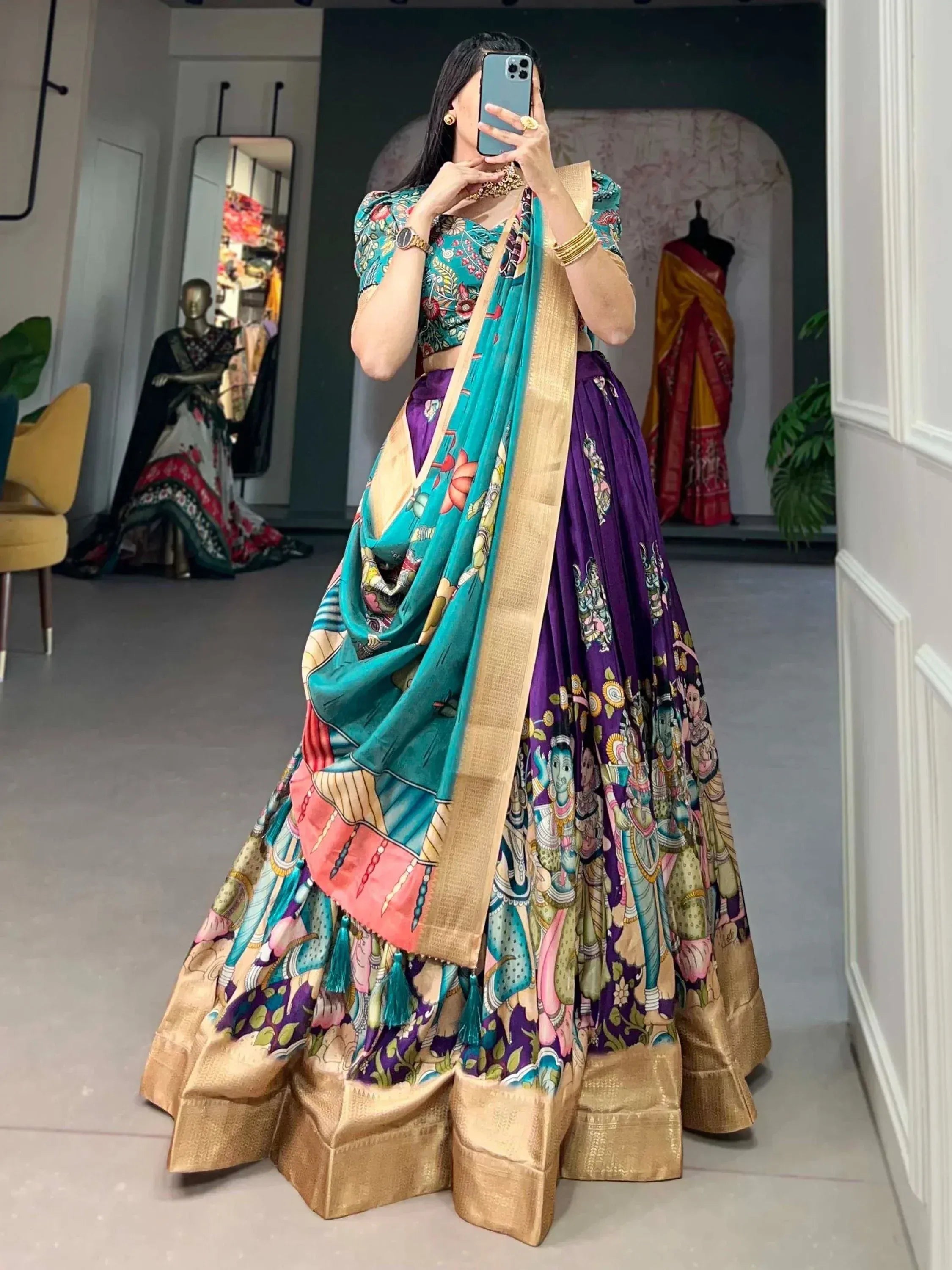 Woman in vibrant purple and teal printed lehenga choli with gold border, taking mirror selfie in boutique