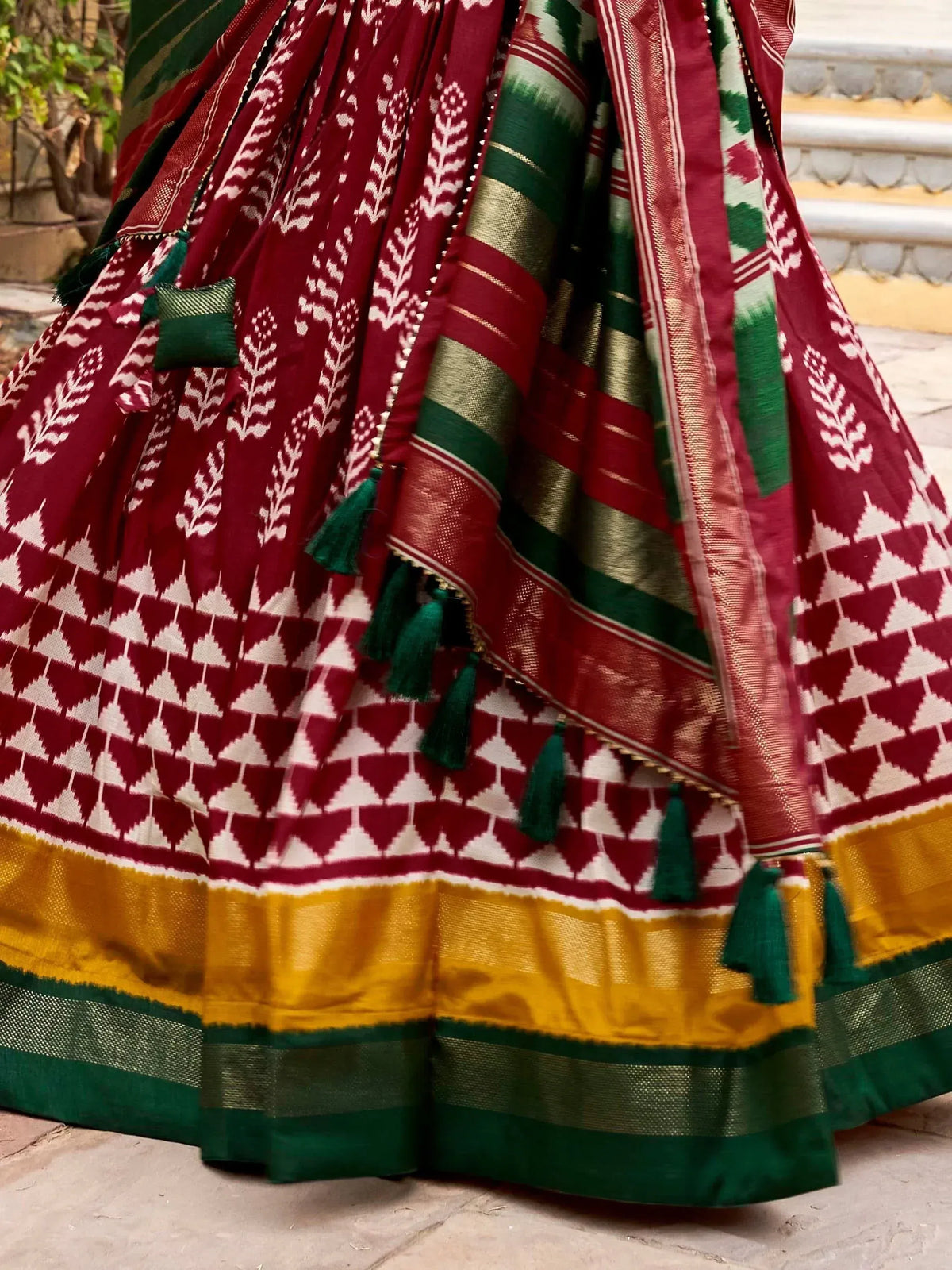 Maroon and green Ikat lehenga with geometric print, gold border, and tassels for ethnic wear