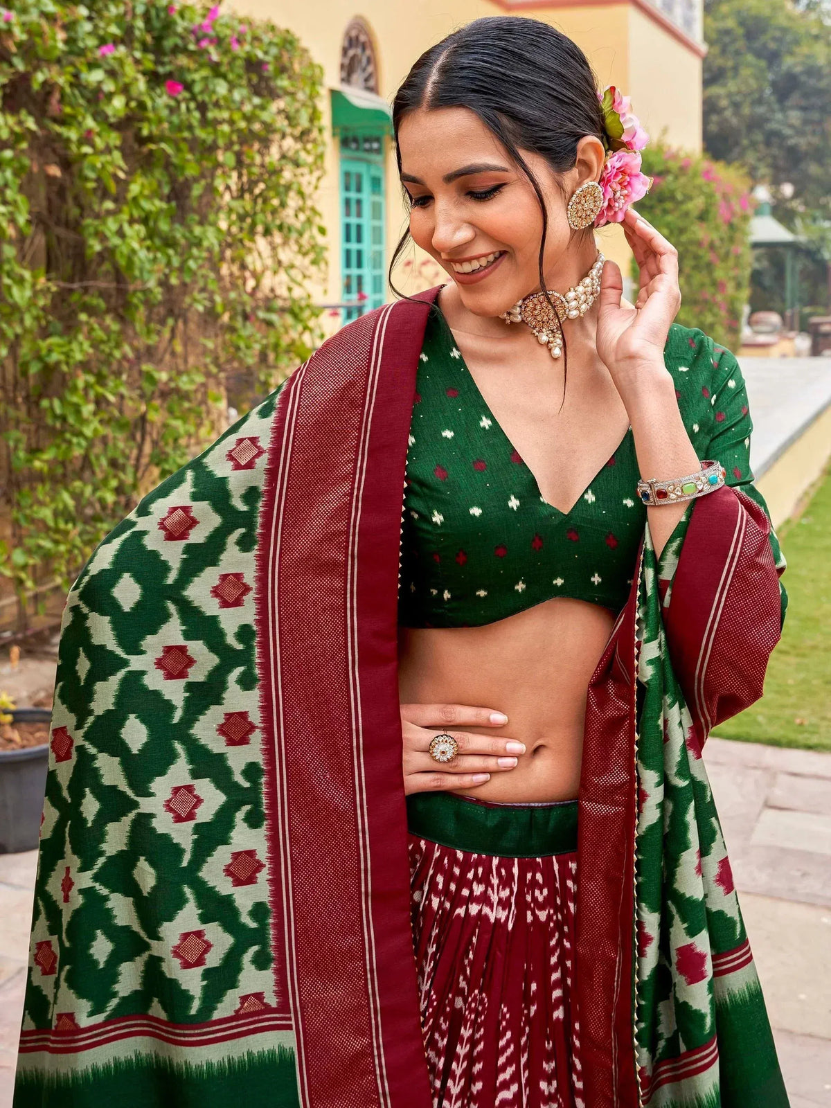 Green and maroon ethnic lehenga choli with ikat dupatta, floral hair accessory, and traditional jewelry