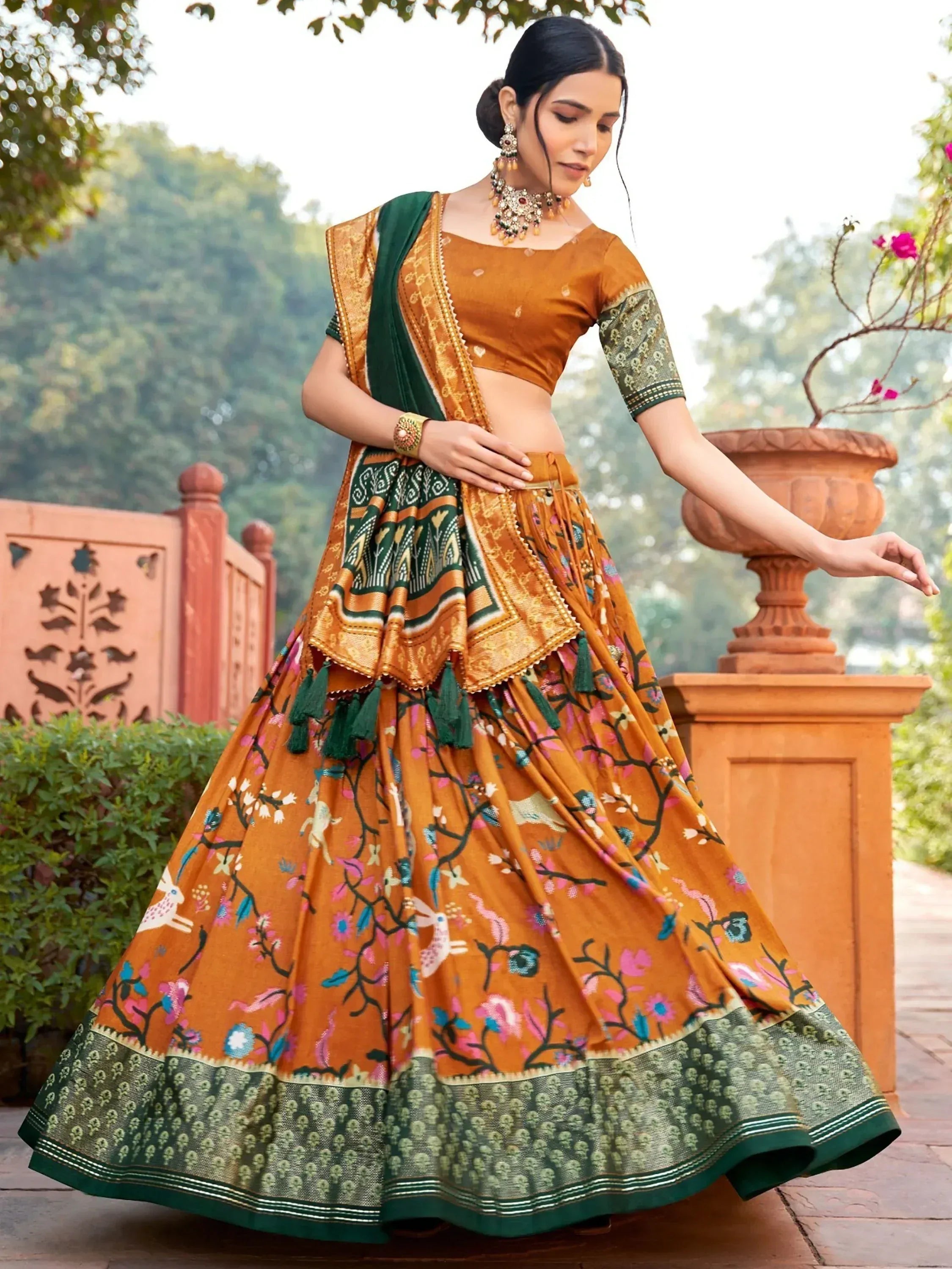 Woman in orange and green printed lehenga choli with floral and animal motifs, perfect for ethnic occasions