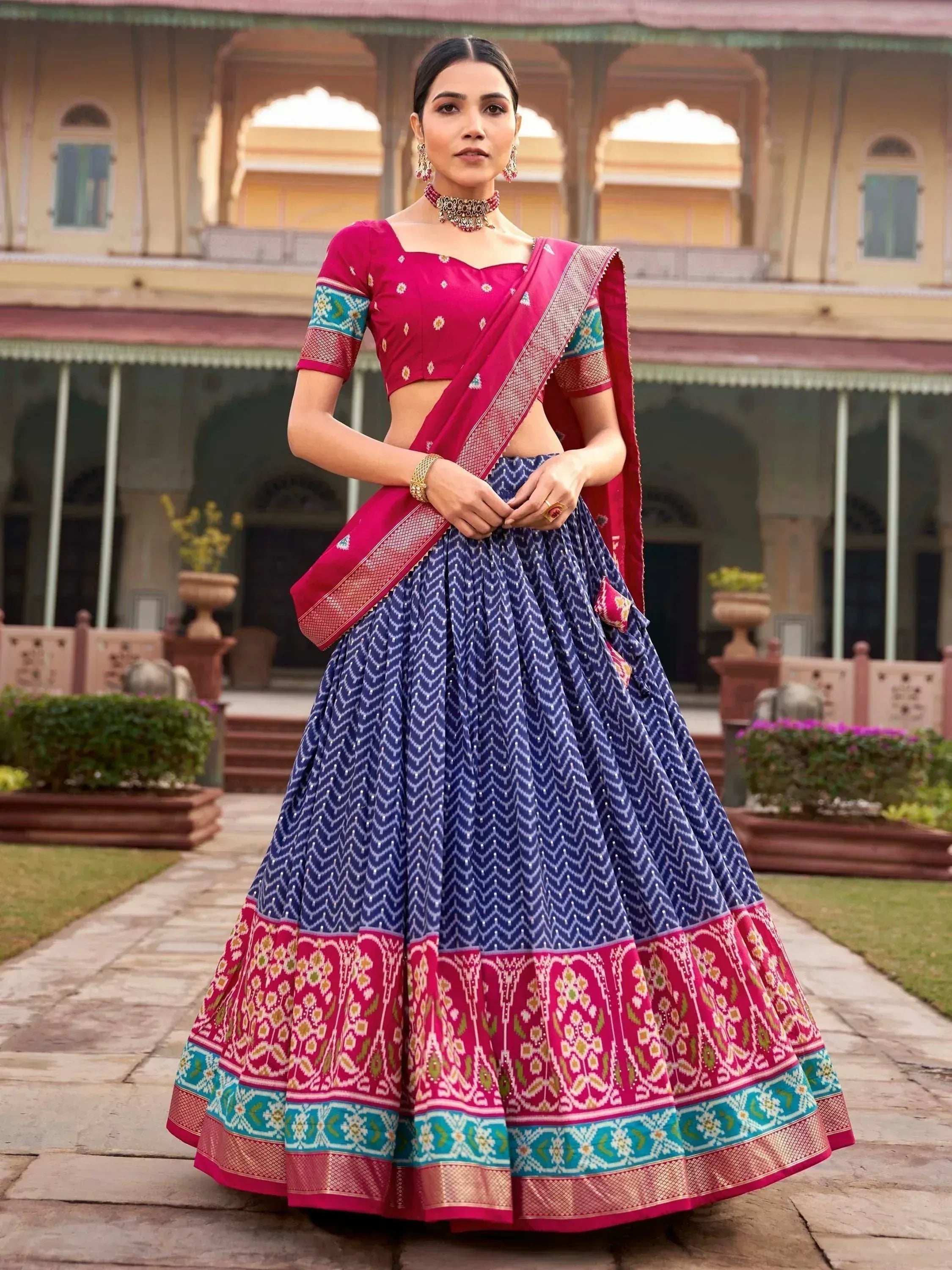 Woman in vibrant pink and blue designer lehenga choli with intricate patterns, perfect for Indian ethnic wear occasions.