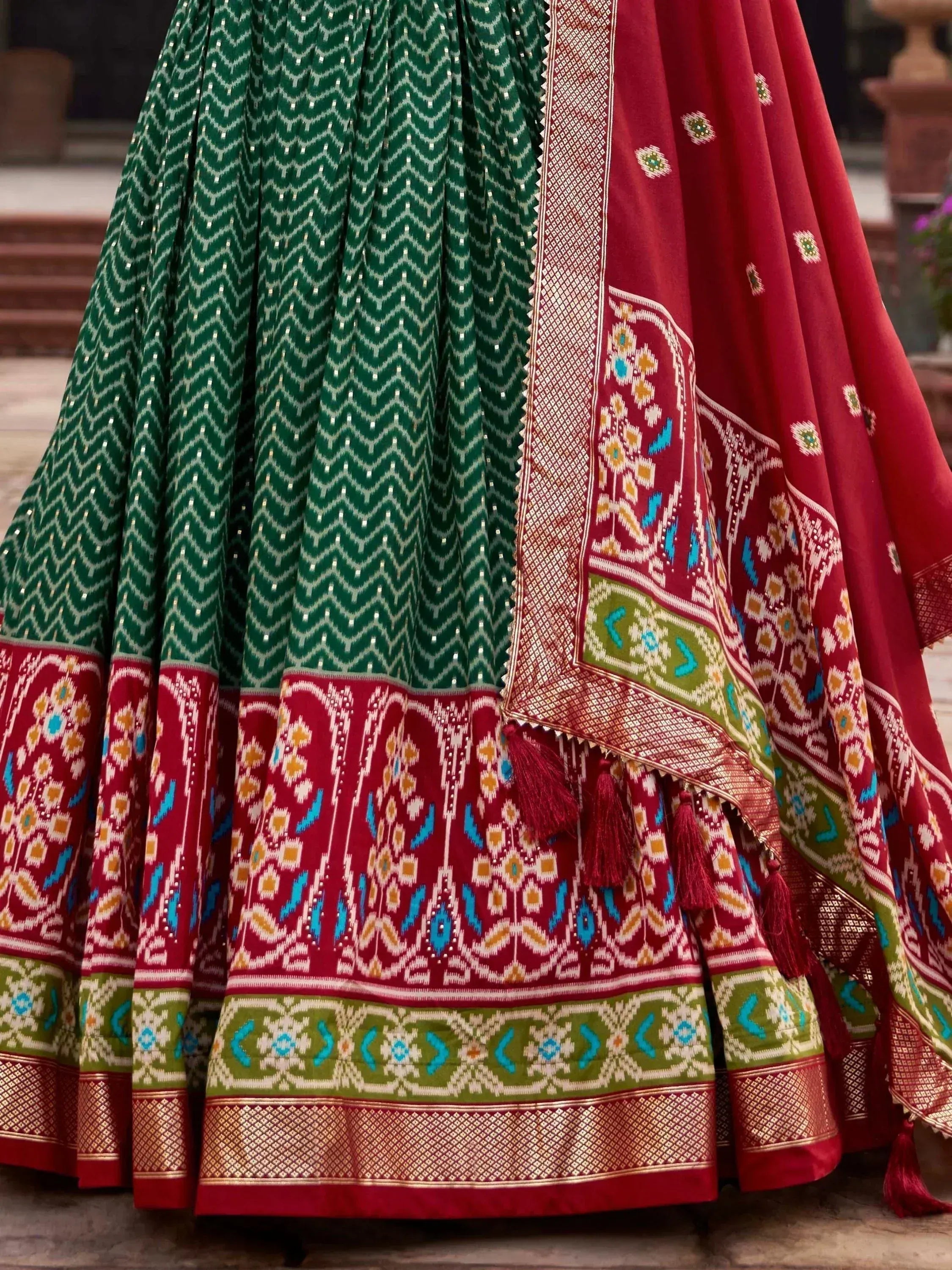 Green and red ethnic lehenga with intricate ikat patterns and tassels, perfect for Indian weddings or festive occasions.