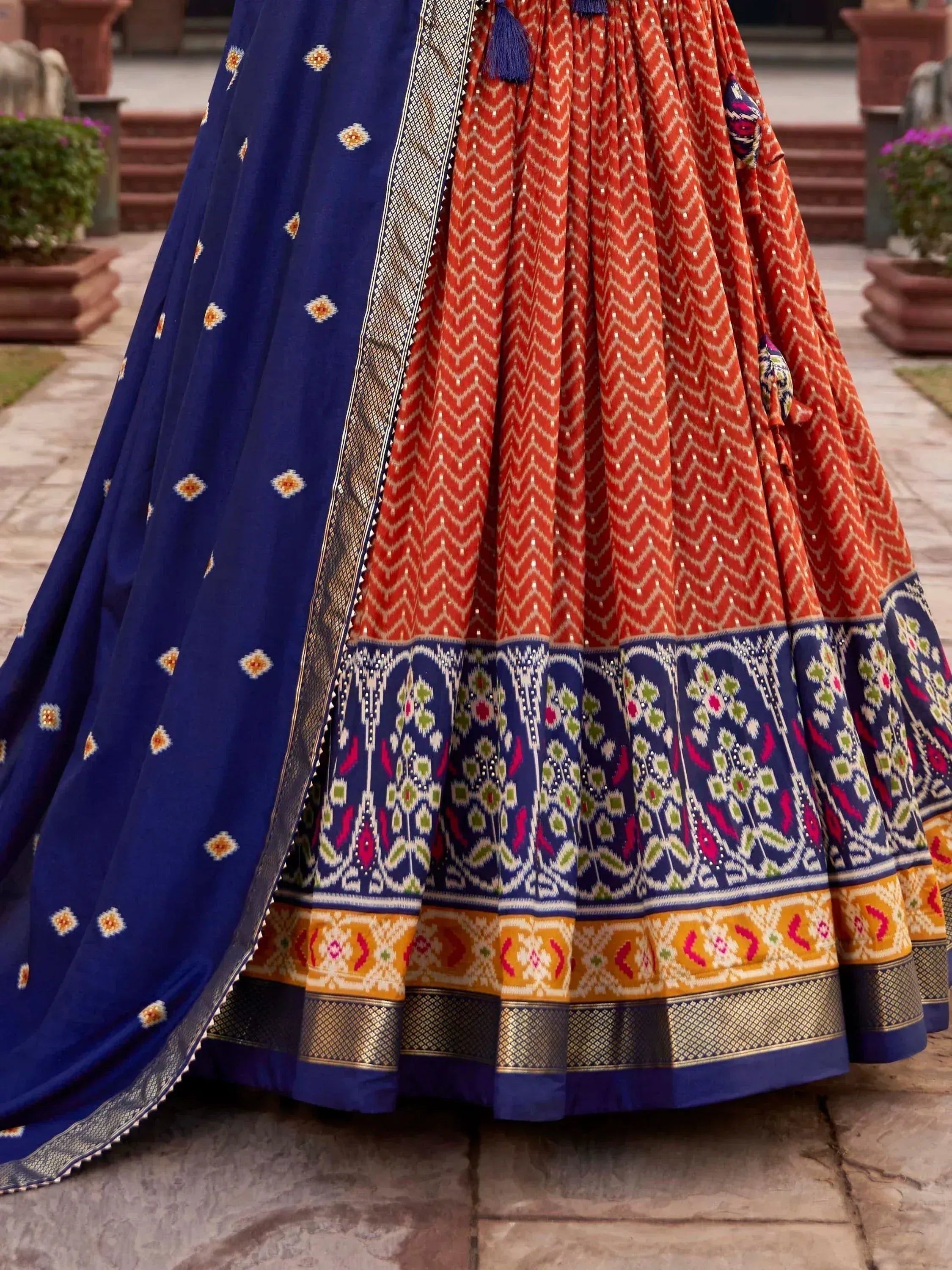 Vibrant orange and blue ethnic lehenga with intricate ikat patterns and gold border, perfect for Indian weddings or festivals.