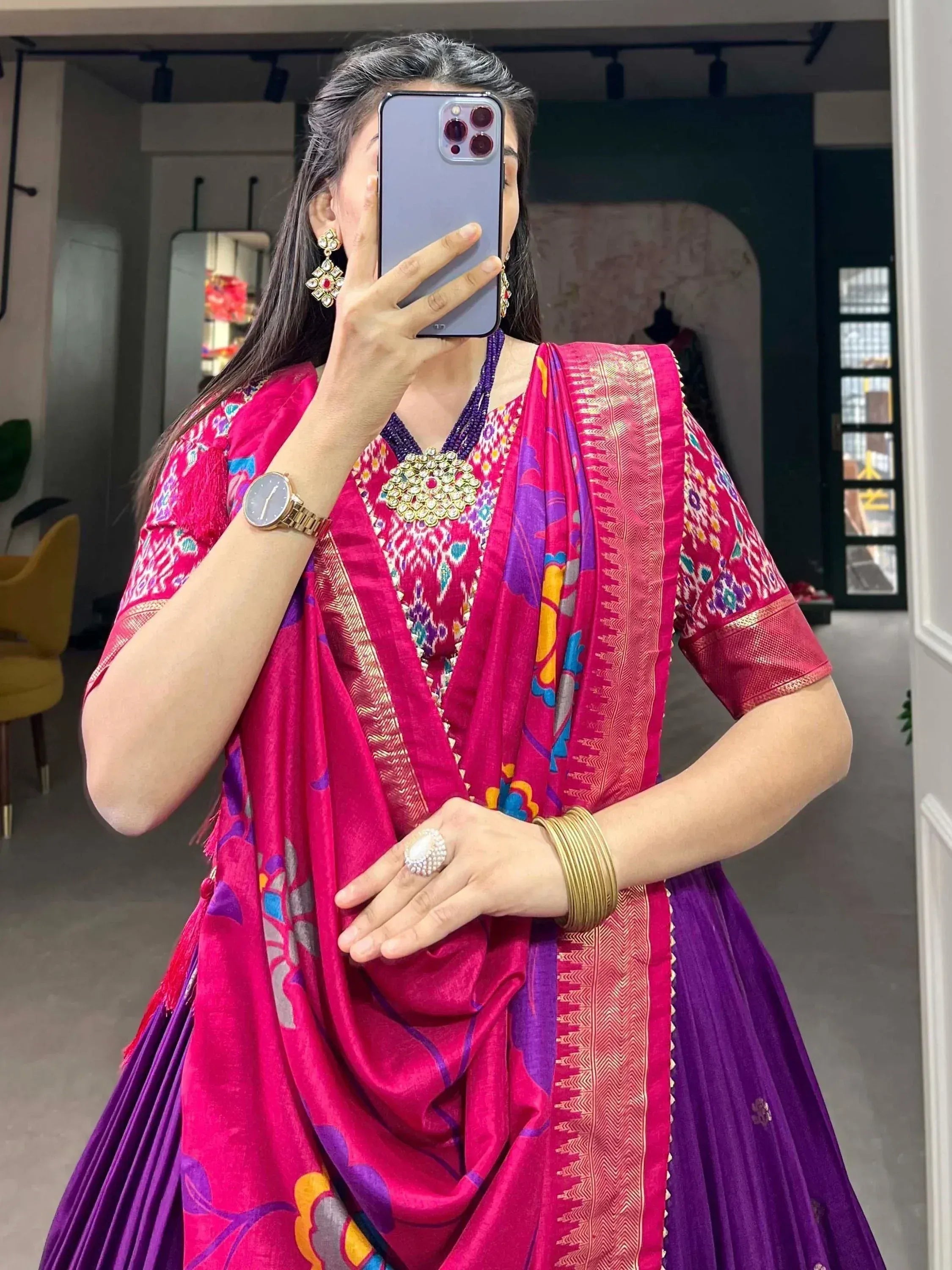 Woman in vibrant pink and purple ethnic lehenga choli with floral print and gold trim, taking mirror selfie