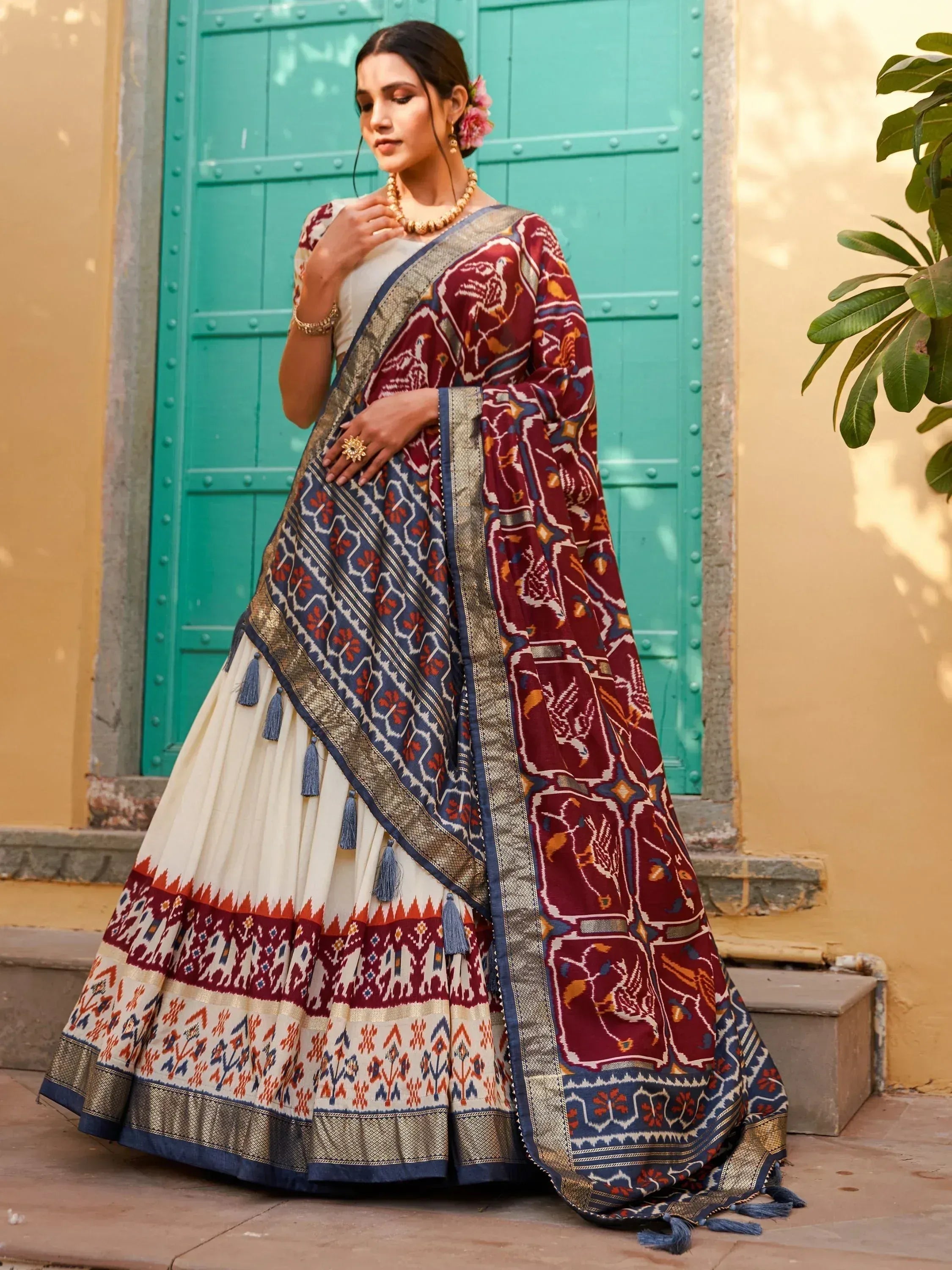 Elegant Indian ethnic saree with intricate maroon and blue patterns, paired with a white blouse and gold jewelry.