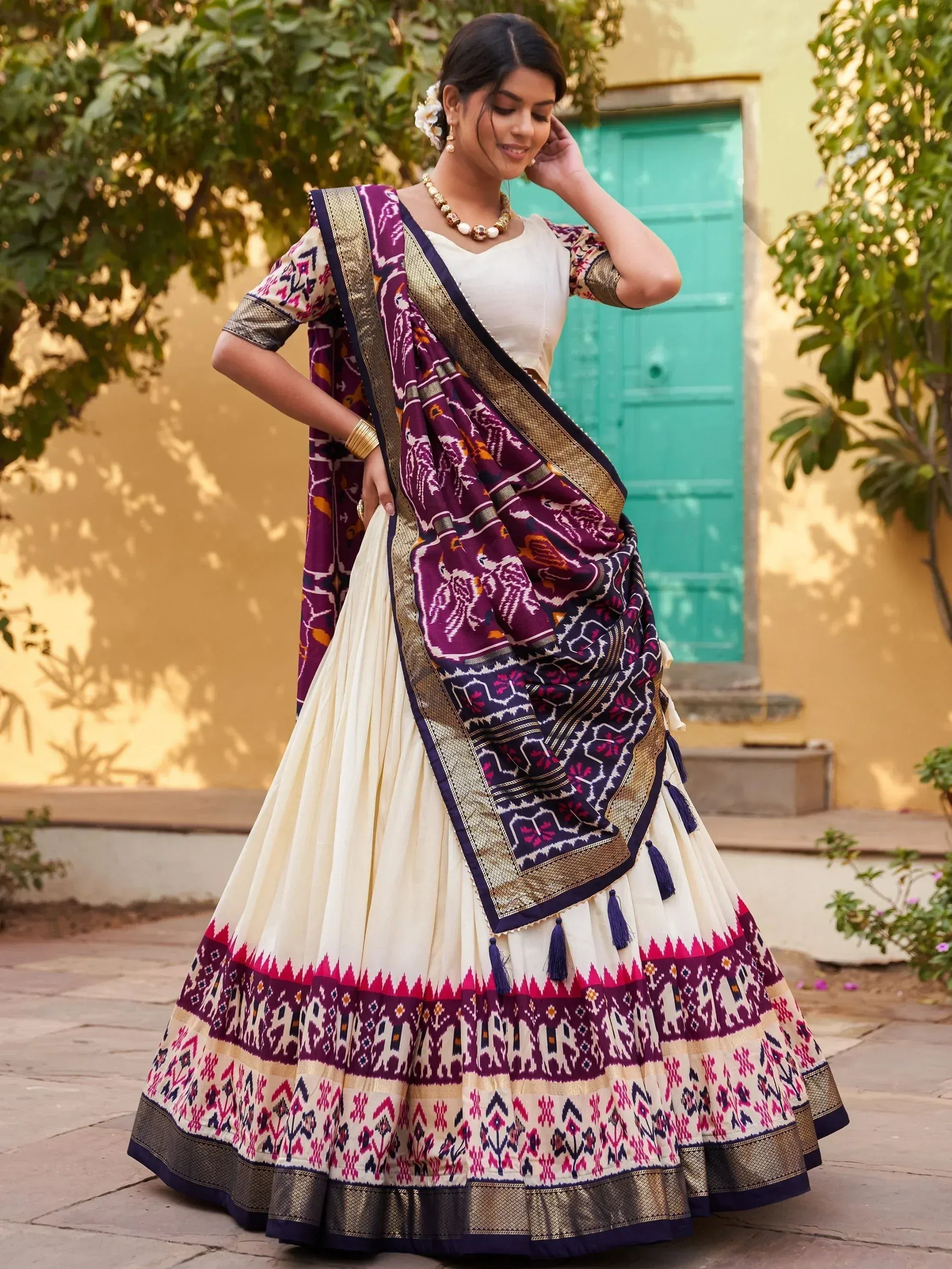 Woman in ethnic Indian lehenga choli with purple ikat dupatta, floral patterns, and gold trim, styled for festive occasions.