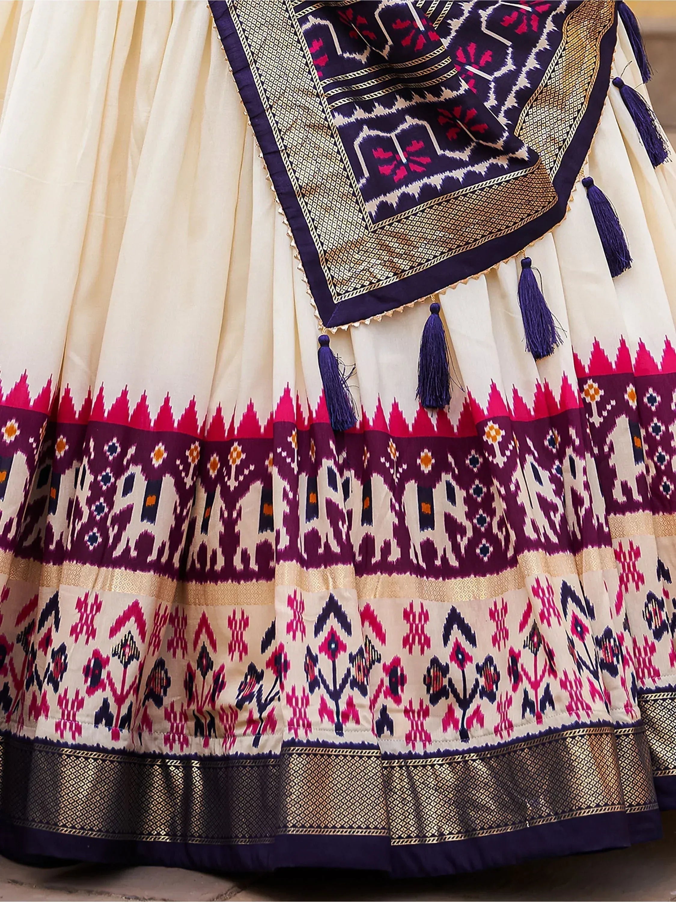 Cream lehenga with purple and pink ikat print, gold border, and tassels, ethnic Indian wear