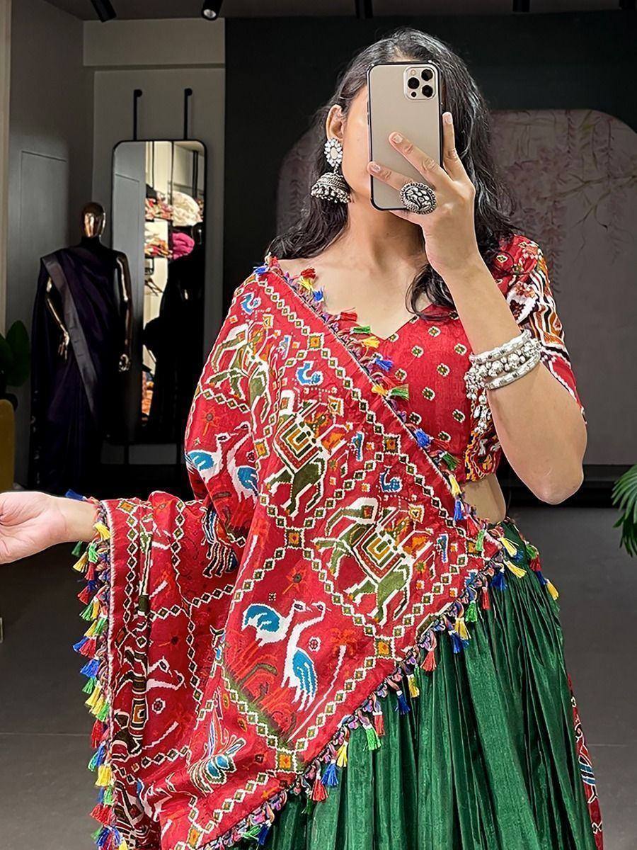 Woman in vibrant red and green ethnic lehenga choli with colorful embroidery and tassels, taking mirror selfie