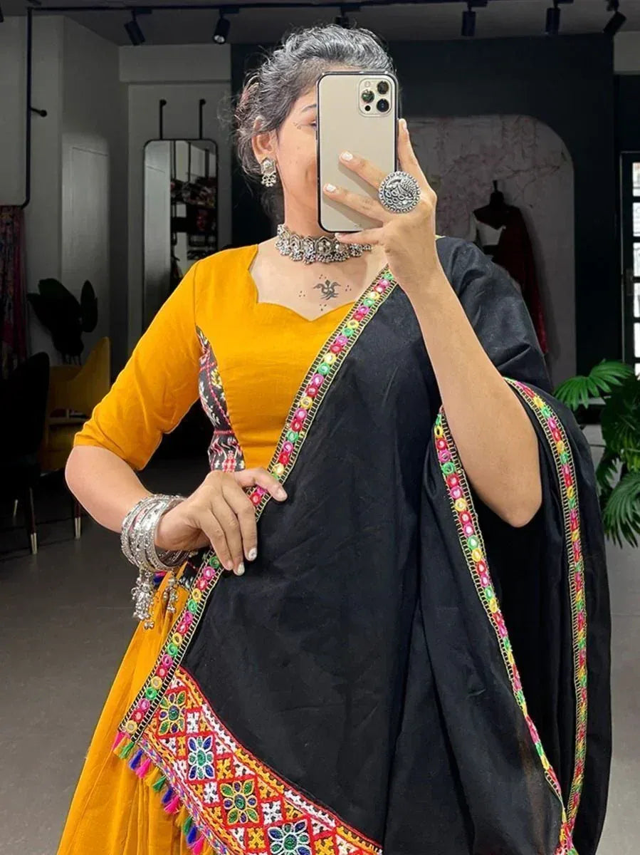 Woman in black saree with colorful embroidery and yellow blouse, taking mirror selfie in boutique