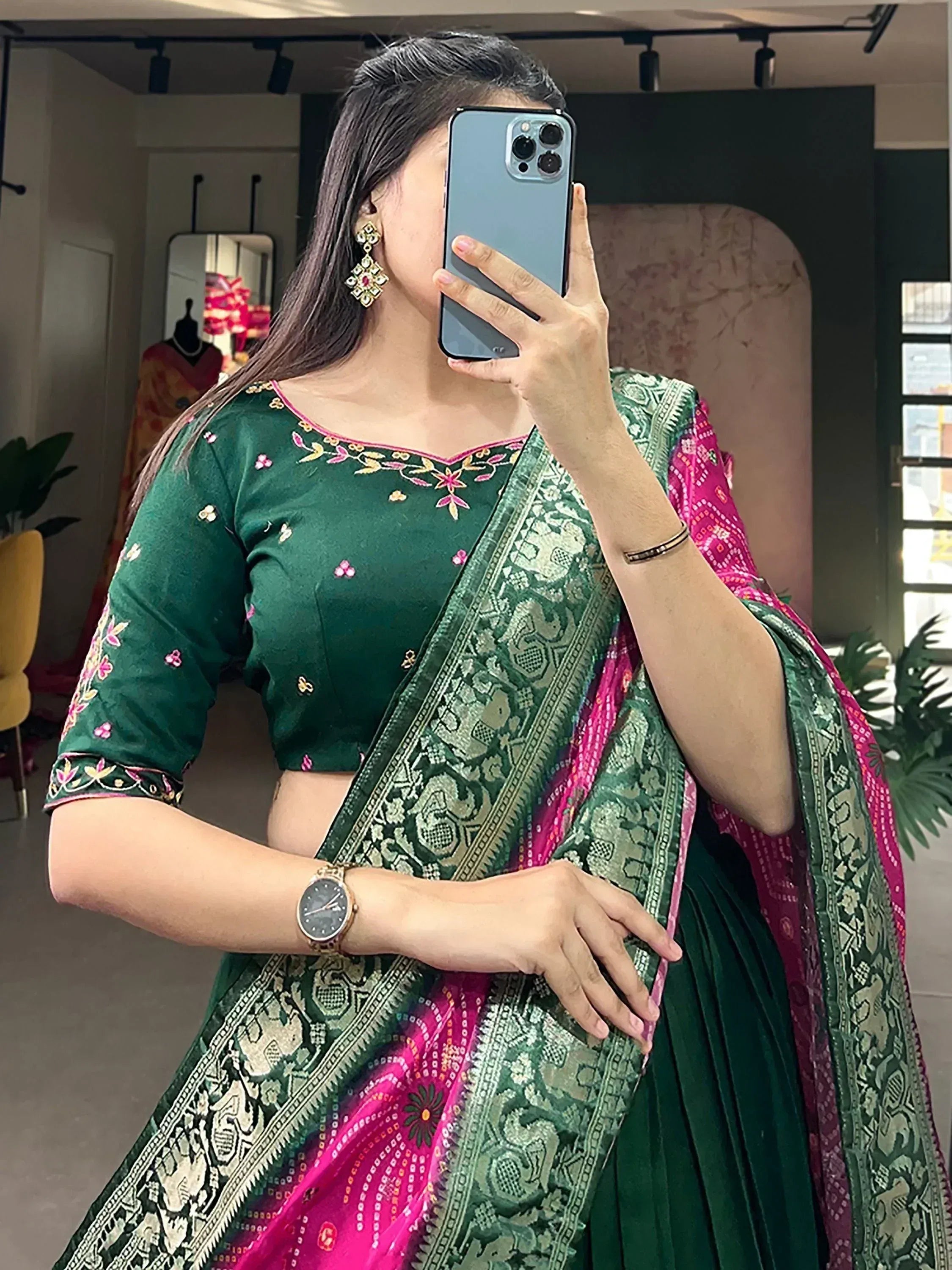 Woman in green embroidered lehenga choli with pink dupatta, taking mirror selfie in boutique
