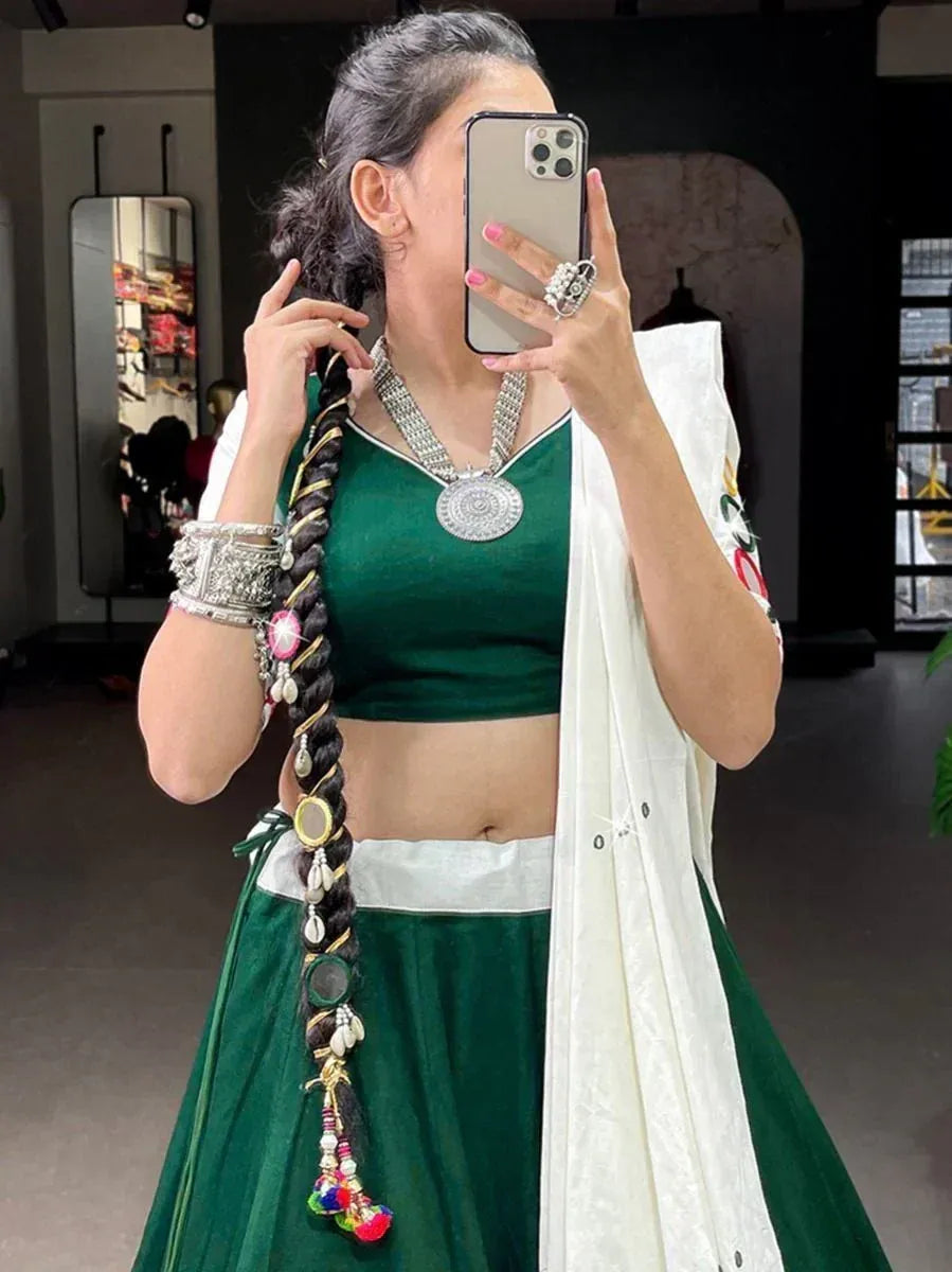 Woman in green lehenga choli with white dupatta, silver jewelry, and decorative braid, taking mirror selfie