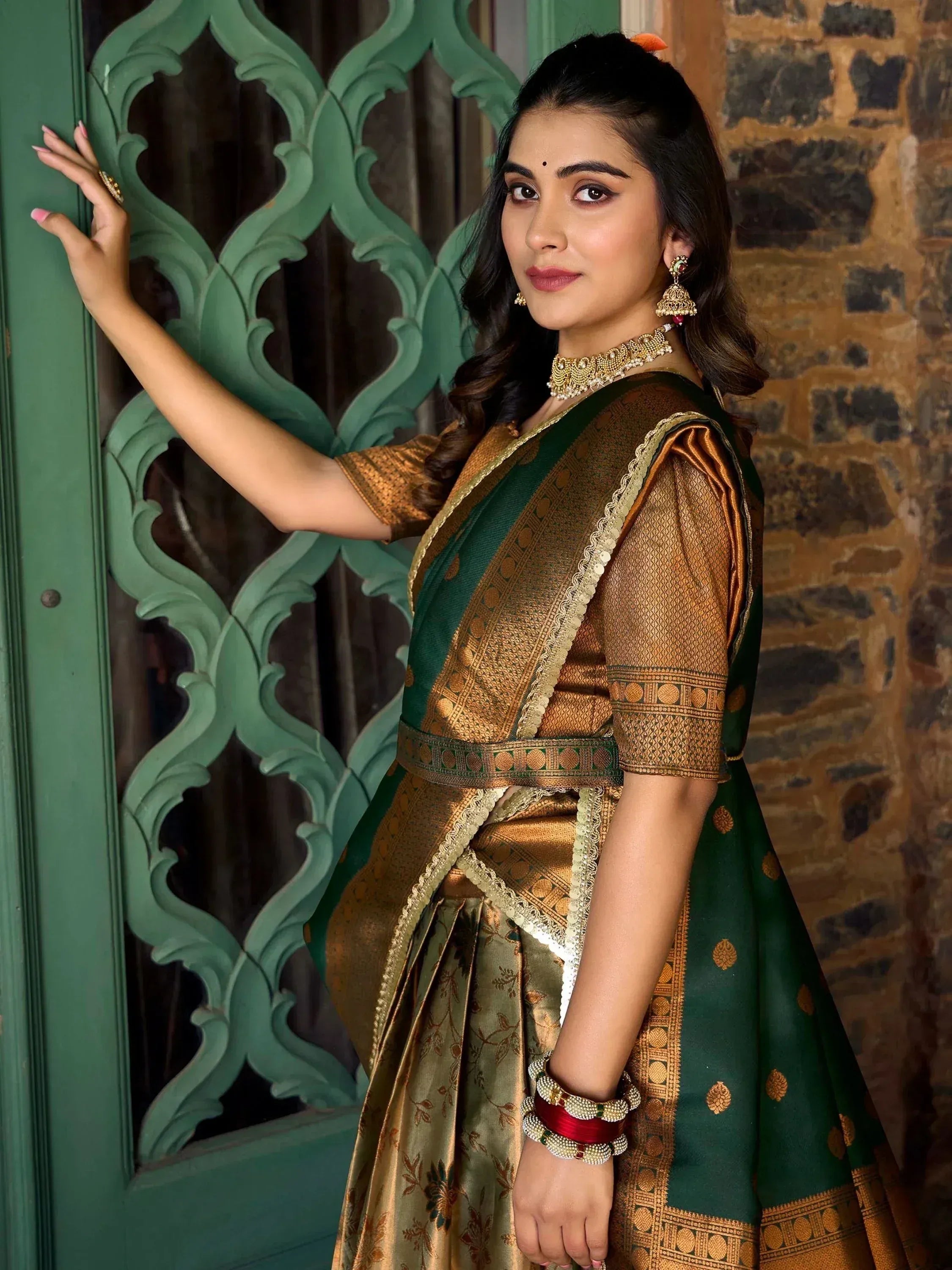 Woman in green and gold designer saree with temple jewelry, posing by ornate door
