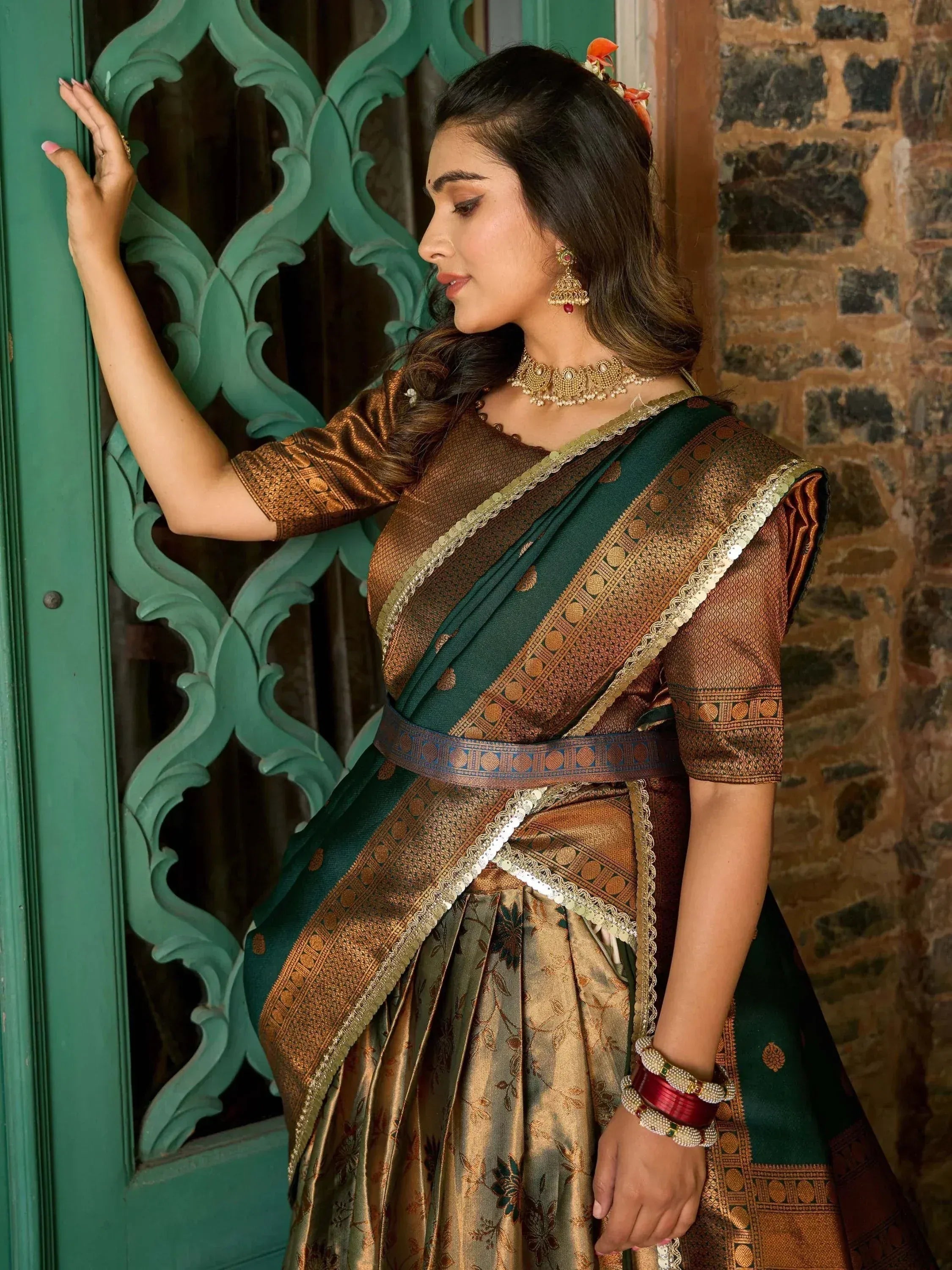 Woman in elegant green and gold designer saree with traditional jewelry, posing by ornate door