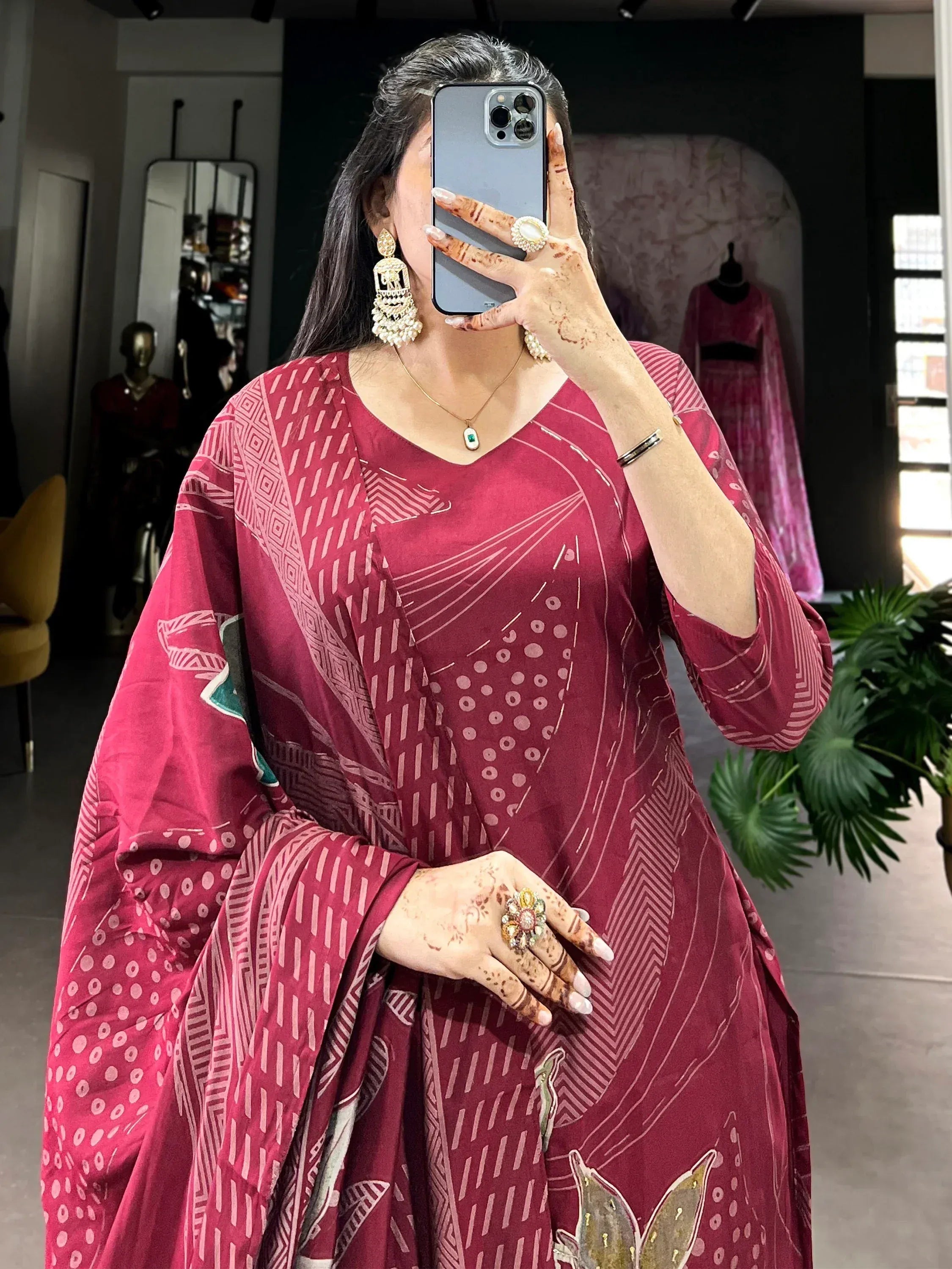 Woman in maroon printed ethnic gown with geometric patterns, henna hands, and statement jewelry