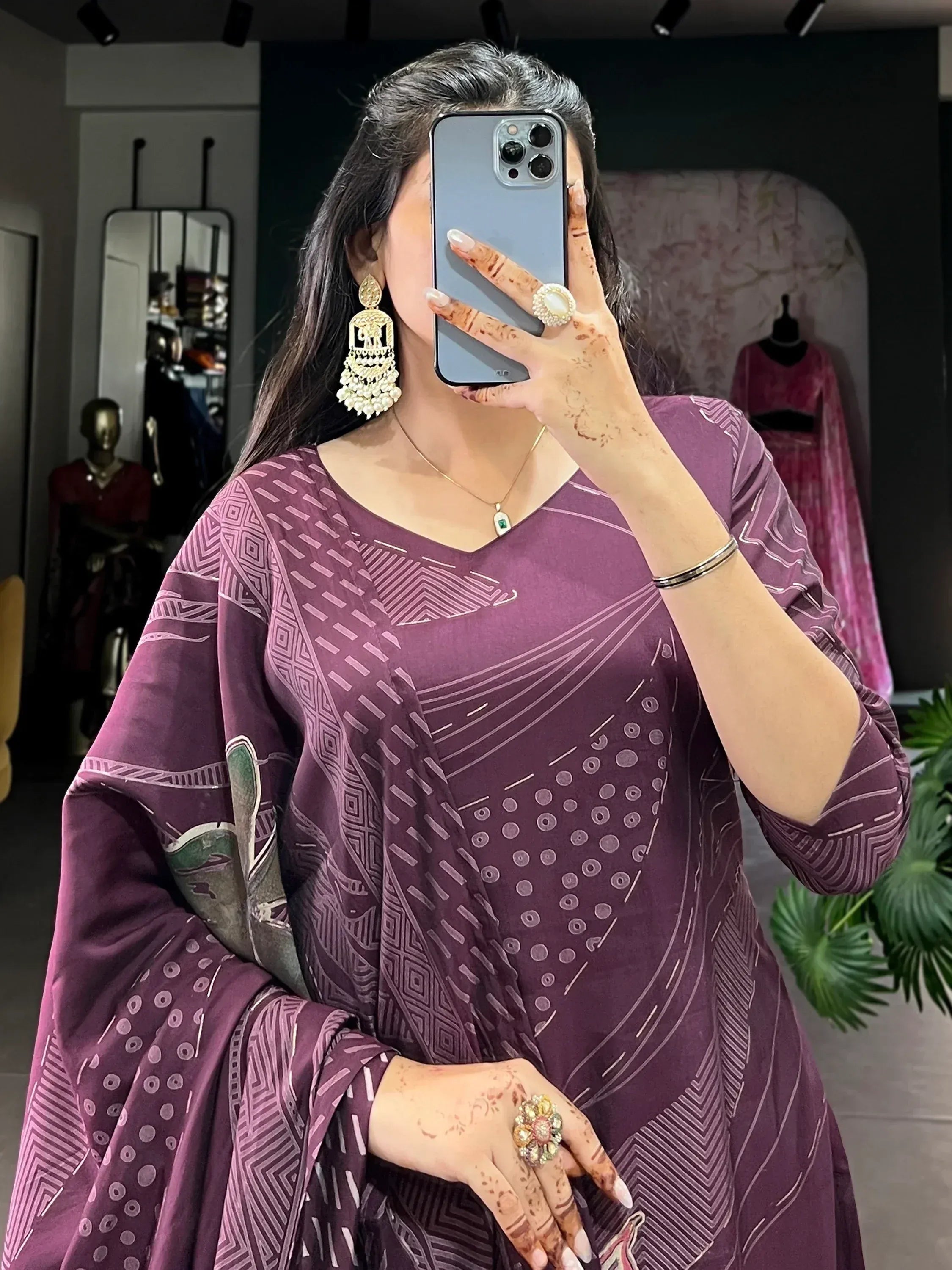 Woman in purple printed ethnic kurta with henna hands, gold jhumka earrings, taking mirror selfie