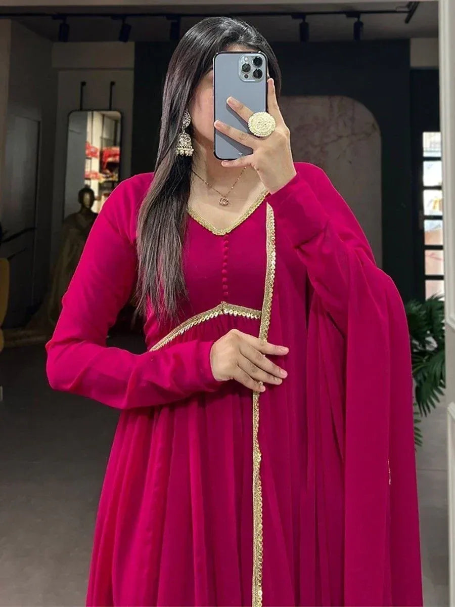Fuchsia ethnic gown with gold trim, long sleeves, and V-neck, styled with jhumka earrings for festive occasions