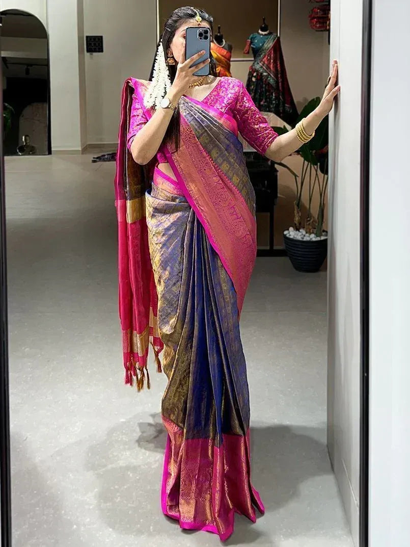 Woman in vibrant pink and blue designer saree with gold embroidery, taking mirror selfie in boutique