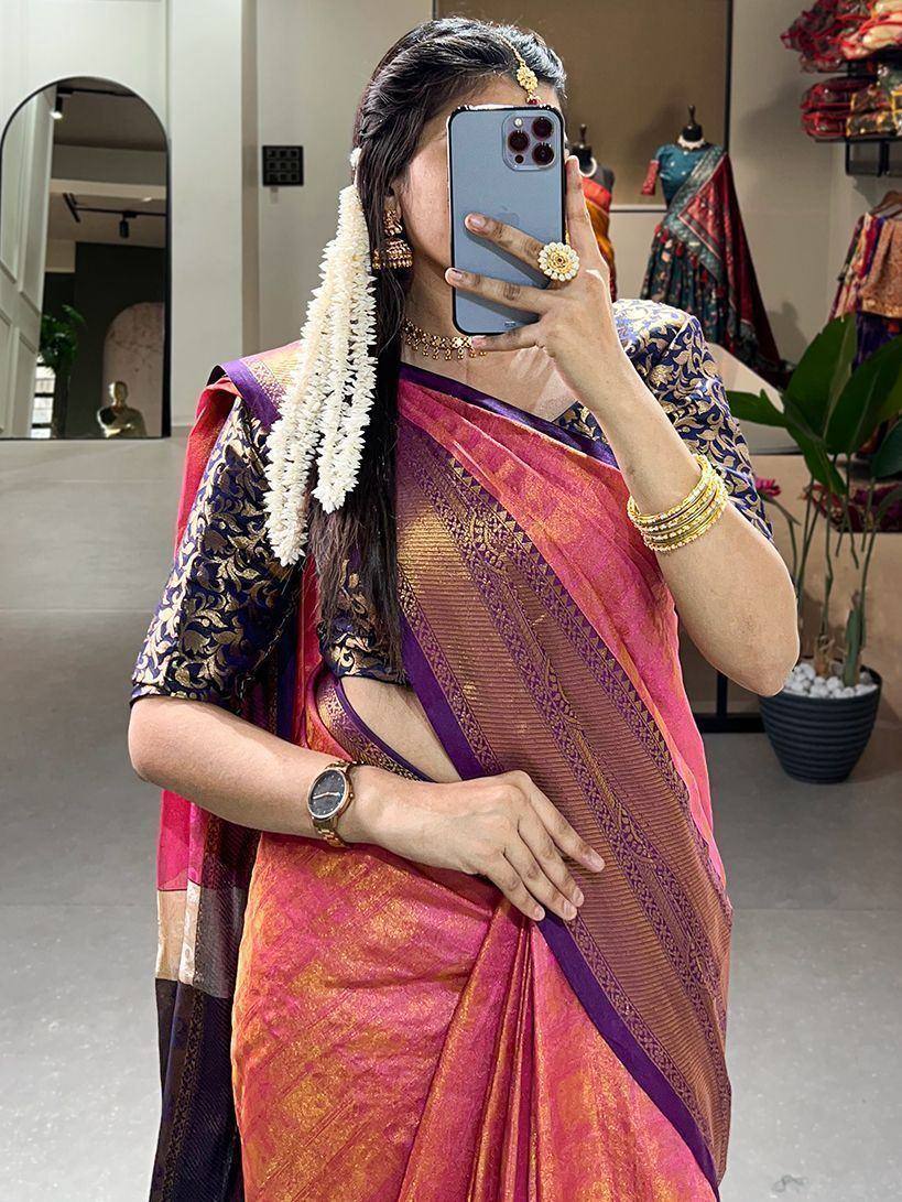 Woman in pink and purple designer saree with gold blouse, floral hair accessory, taking mirror selfie