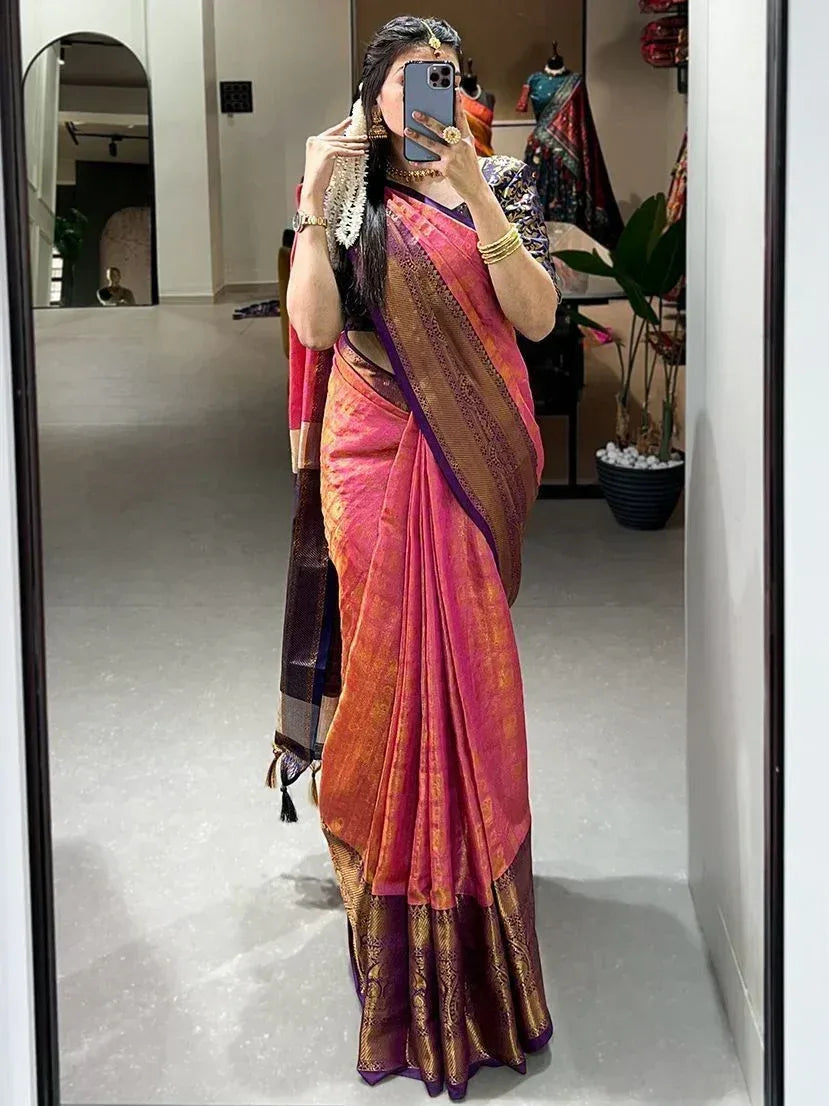 Woman in vibrant pink and gold designer saree with purple border, taking mirror selfie in boutique