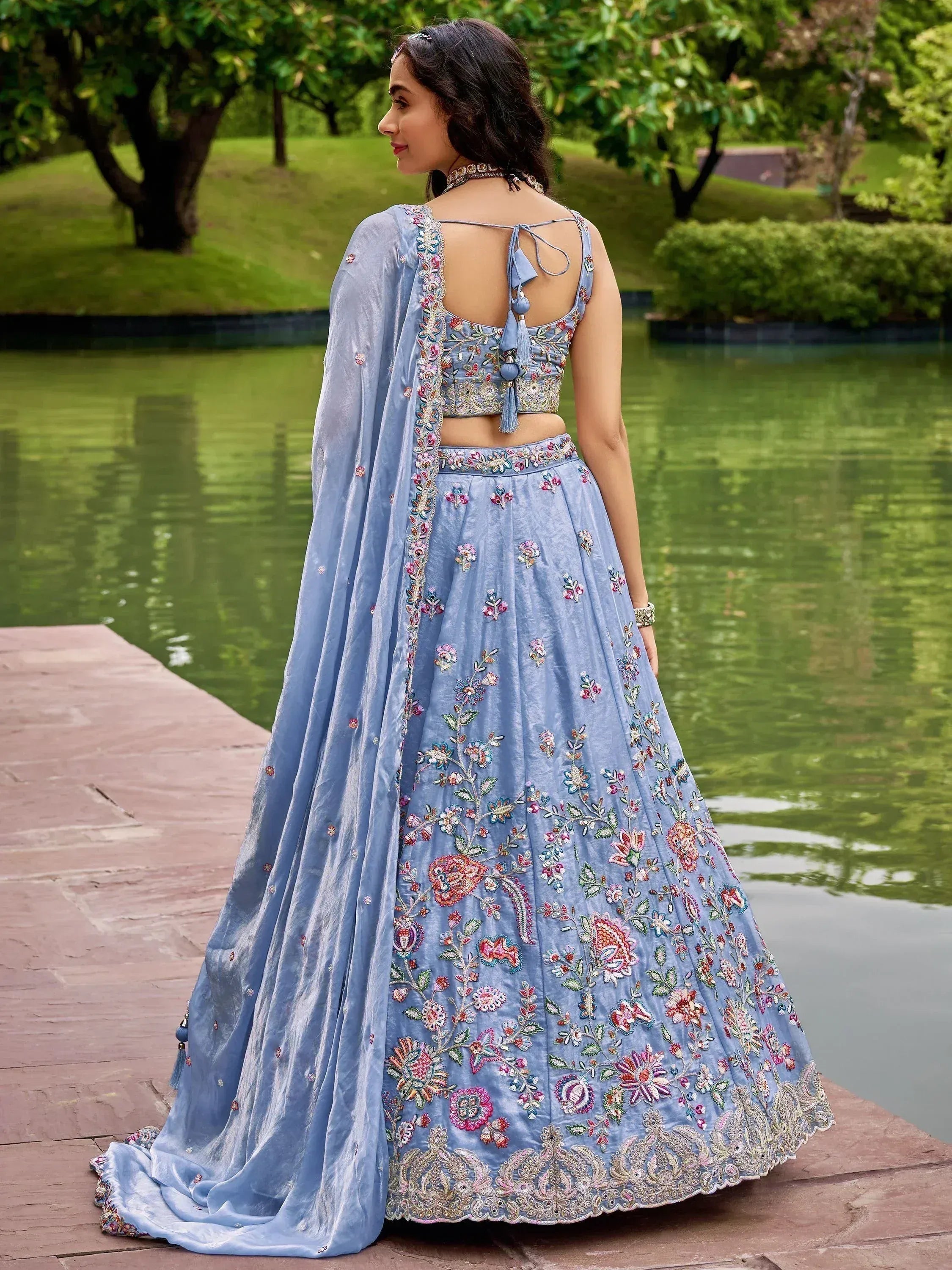 Light blue embroidered lehenga choli with floral motifs, back view by water garden