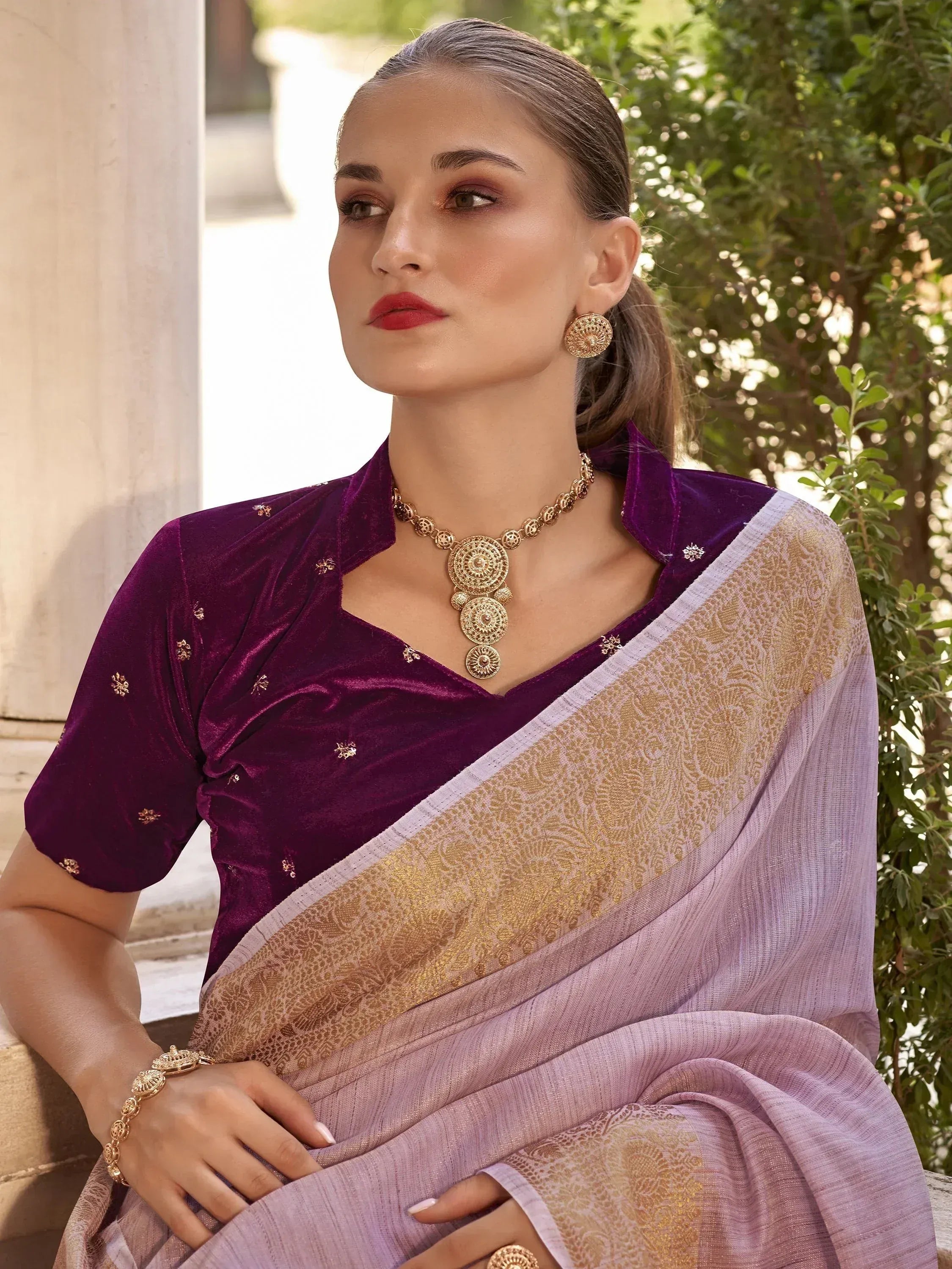 Woman in purple velvet blouse and lavender saree with gold embroidery, styled with traditional Indian jewelry.
