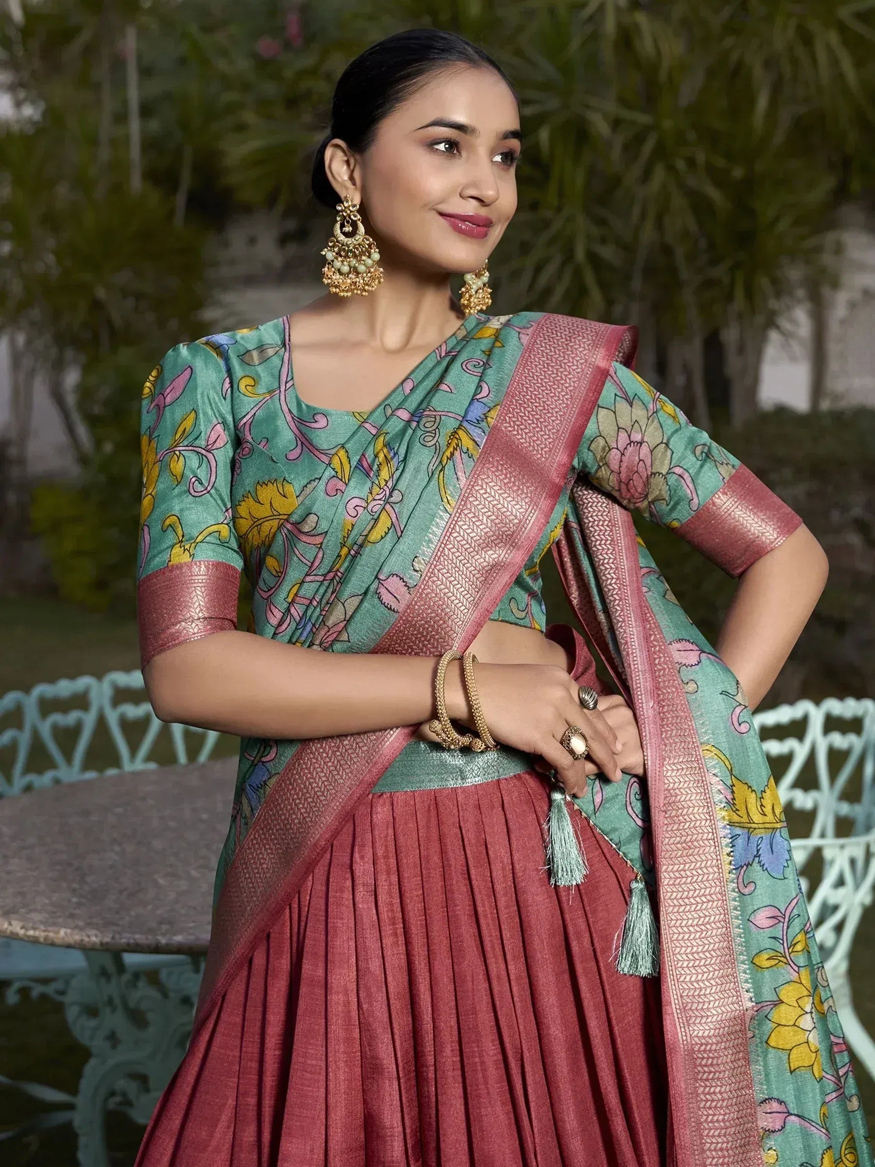 Woman in floral printed green and pink lehenga choli with gold jewelry, garden setting