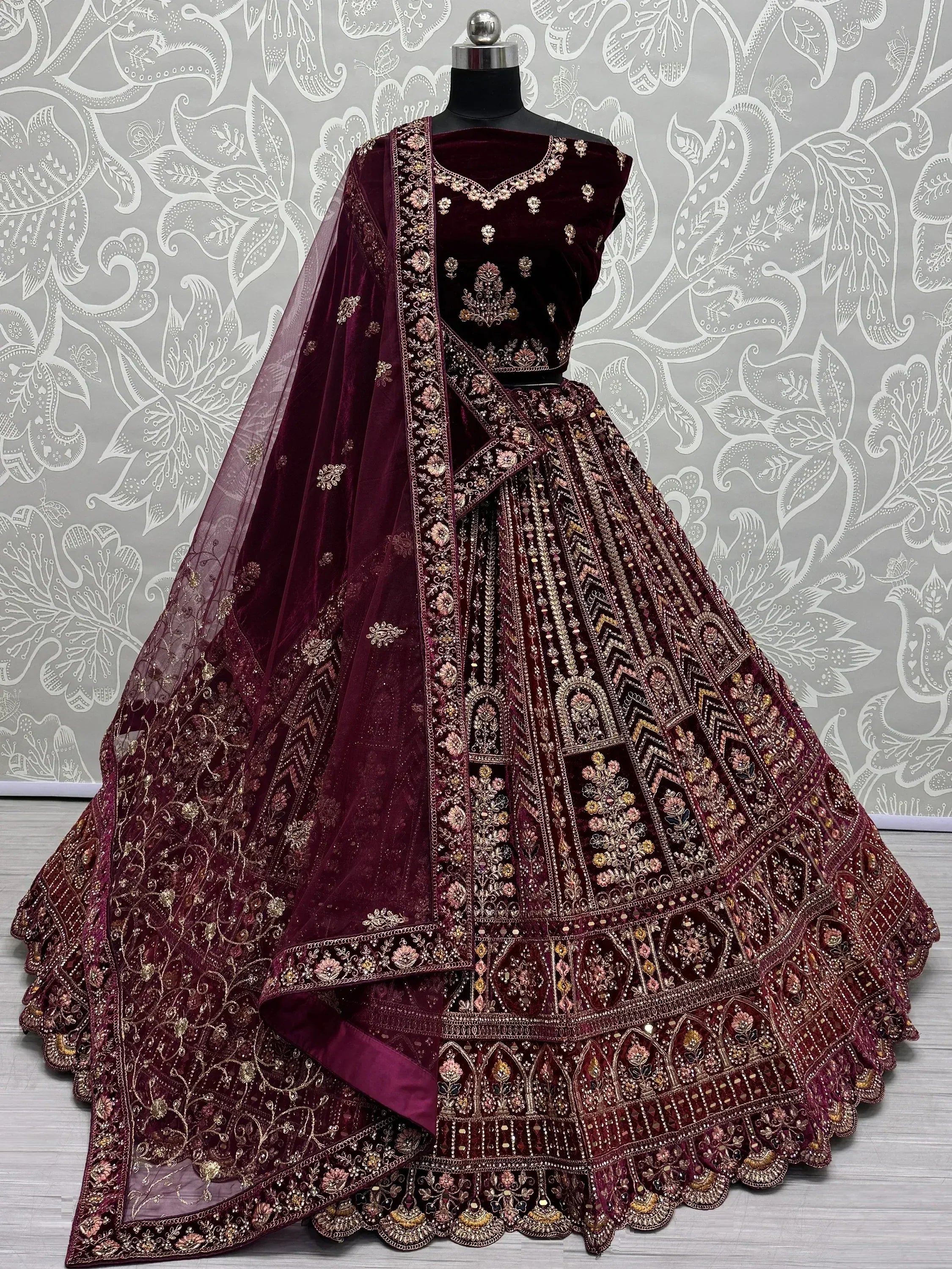 Burgundy velvet lehenga choli with heavy gold embroidery and sheer dupatta, ideal for weddings and festive occasions.