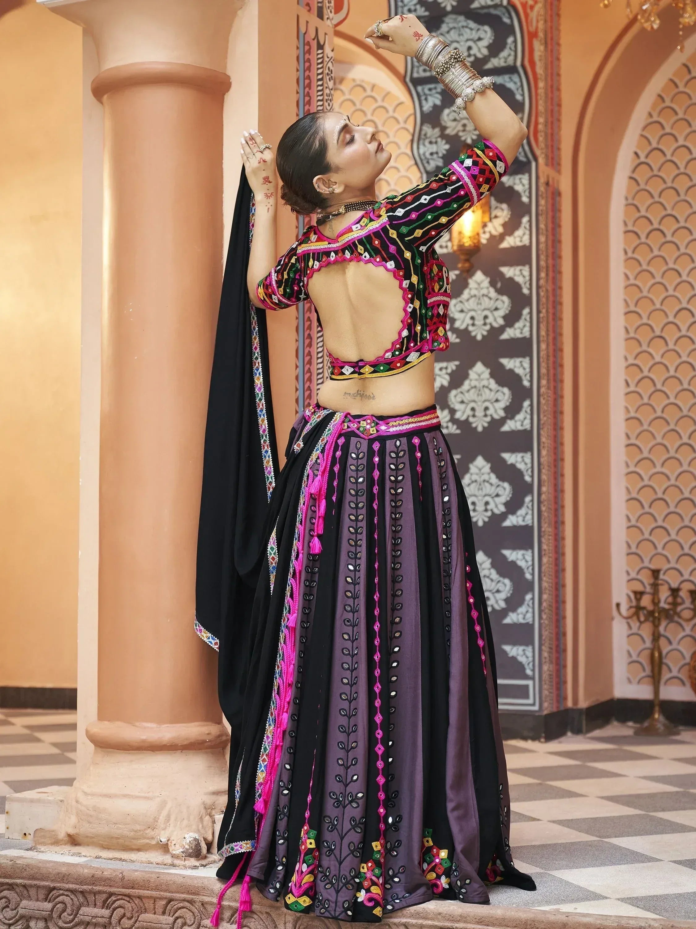 Woman in colorful embroidered Indian ethnic wear with backless top and flared skirt, posing near ornate pillar