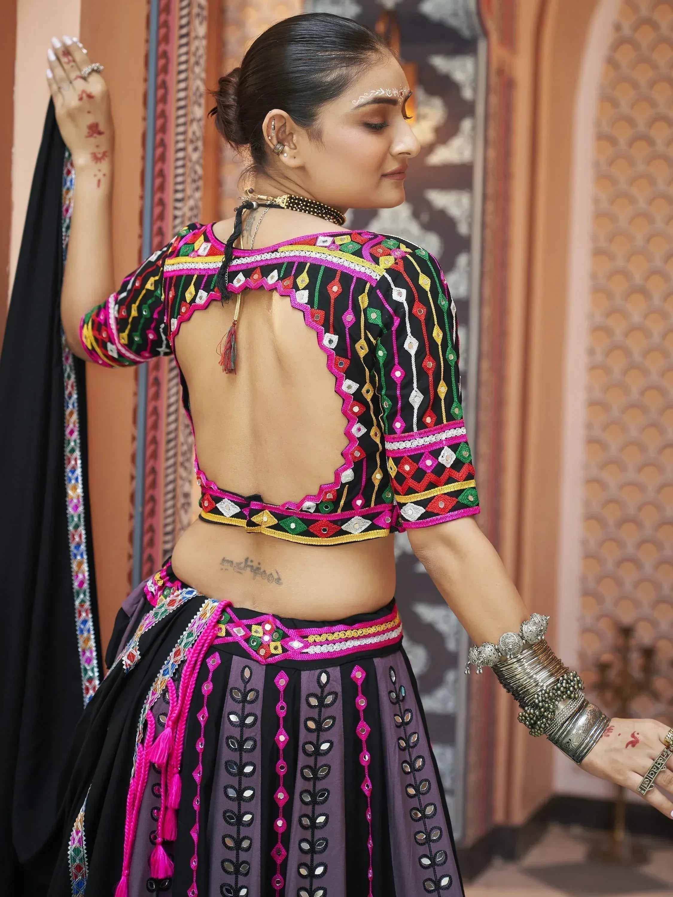 Black and purple ethnic lehenga choli with colorful mirror work, backless blouse, and traditional jewelry