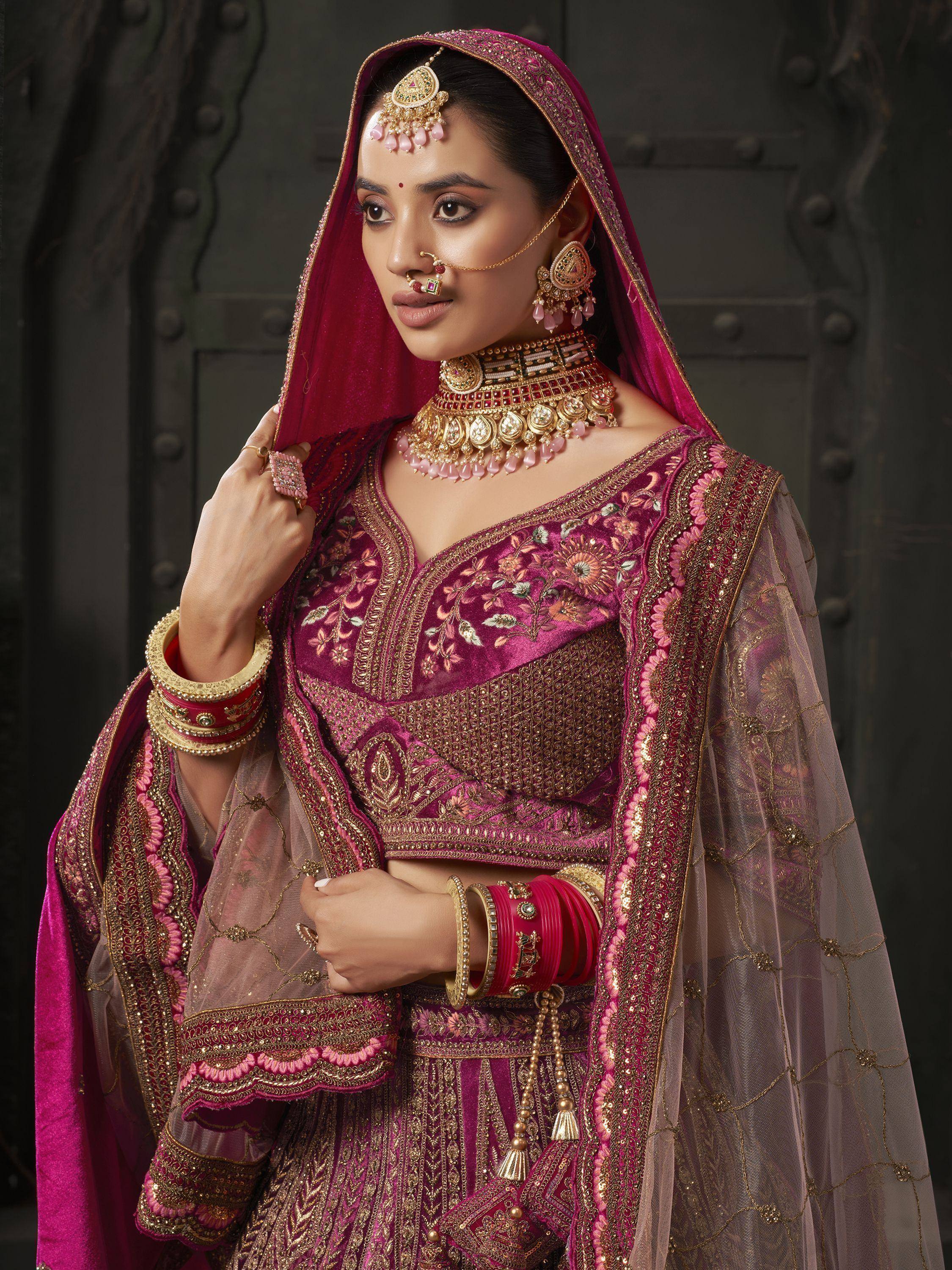 Elegant Indian bridal lehenga choli in magenta with gold embroidery, paired with traditional jewelry and dupatta.