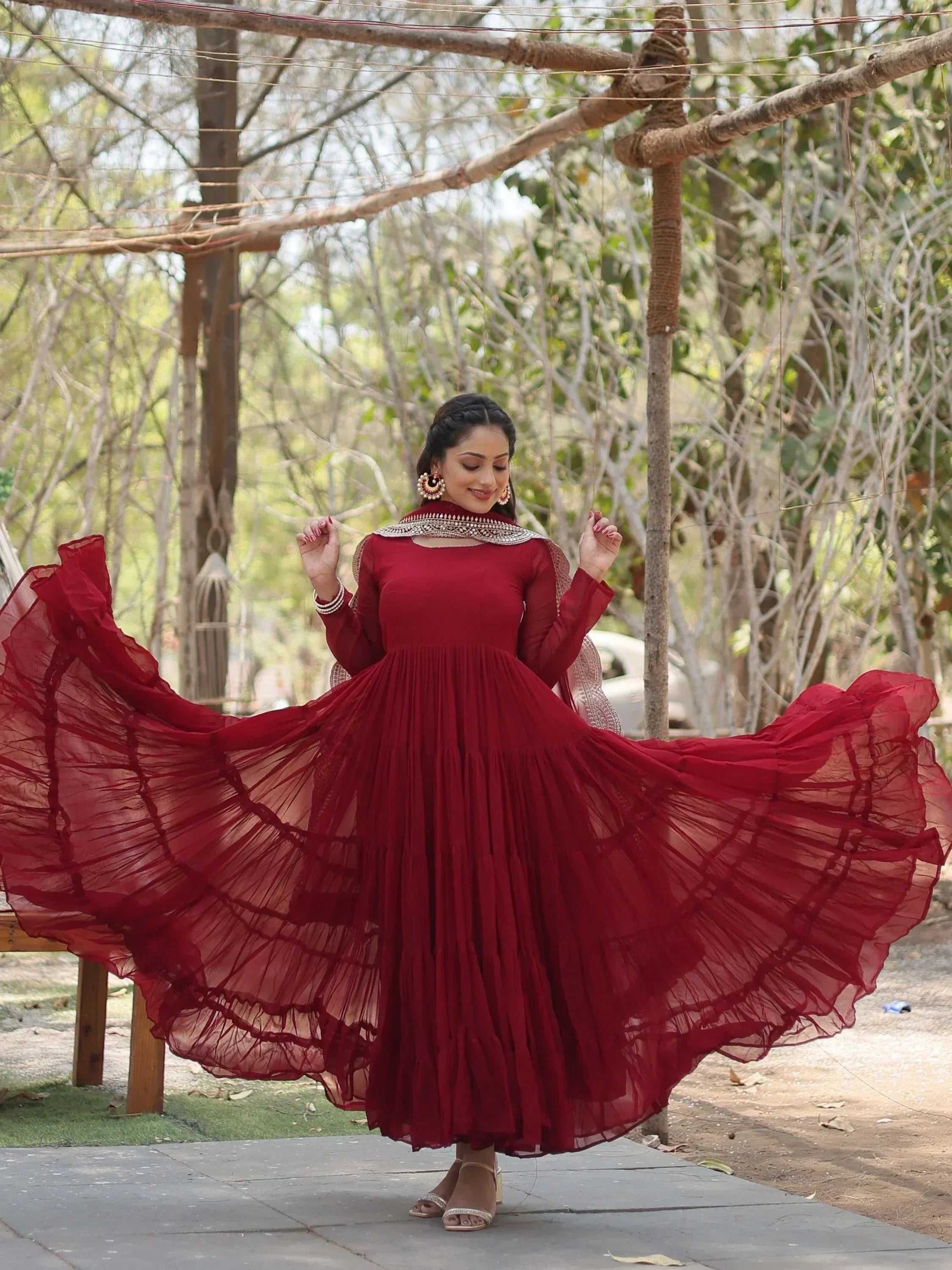 Woman wearing a flowy maroon Anarkali gown with dupatta, posing outdoors