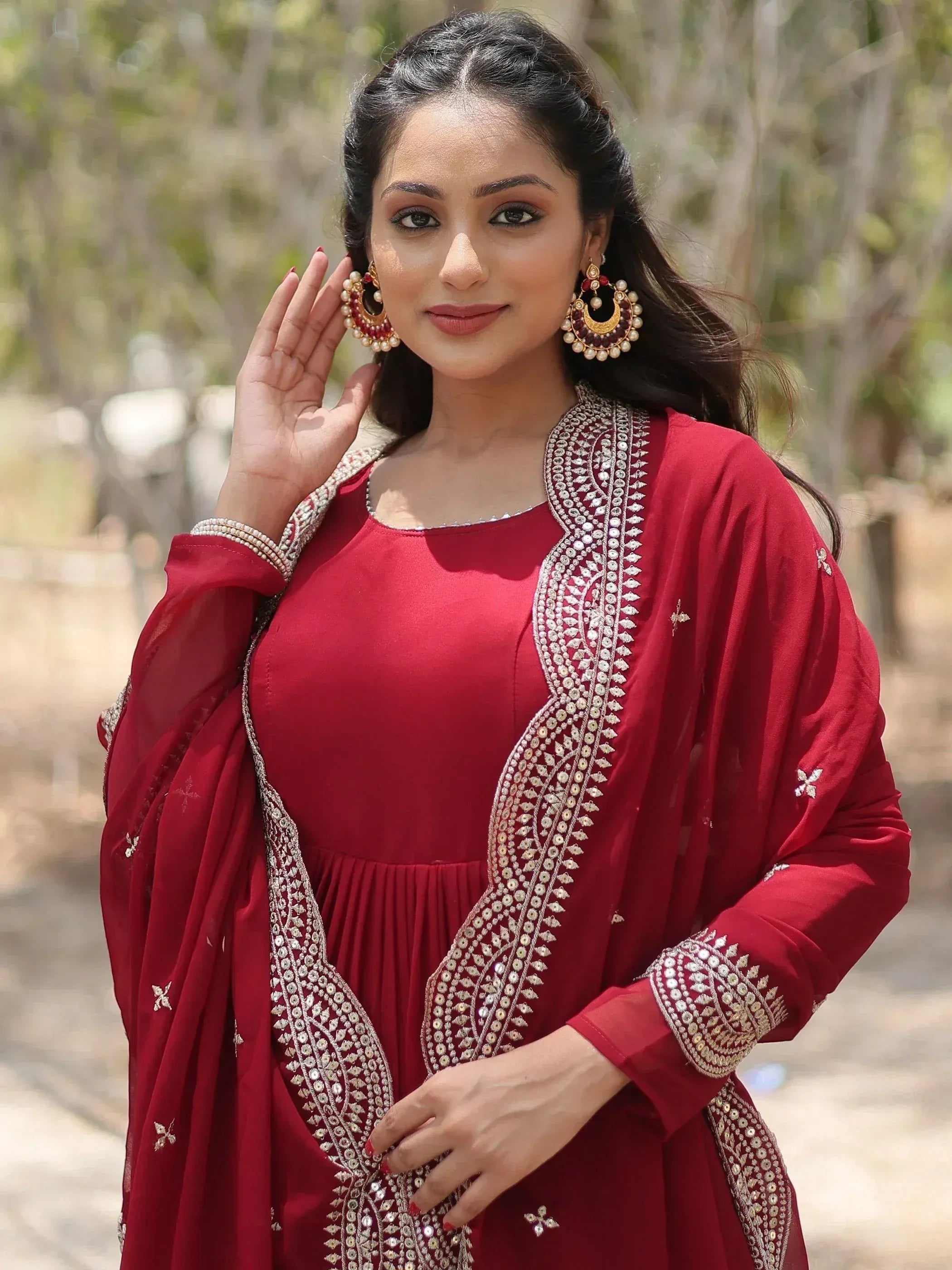 Woman wearing maroon embroidered ethnic gown with dupatta and traditional jewelry outdoors