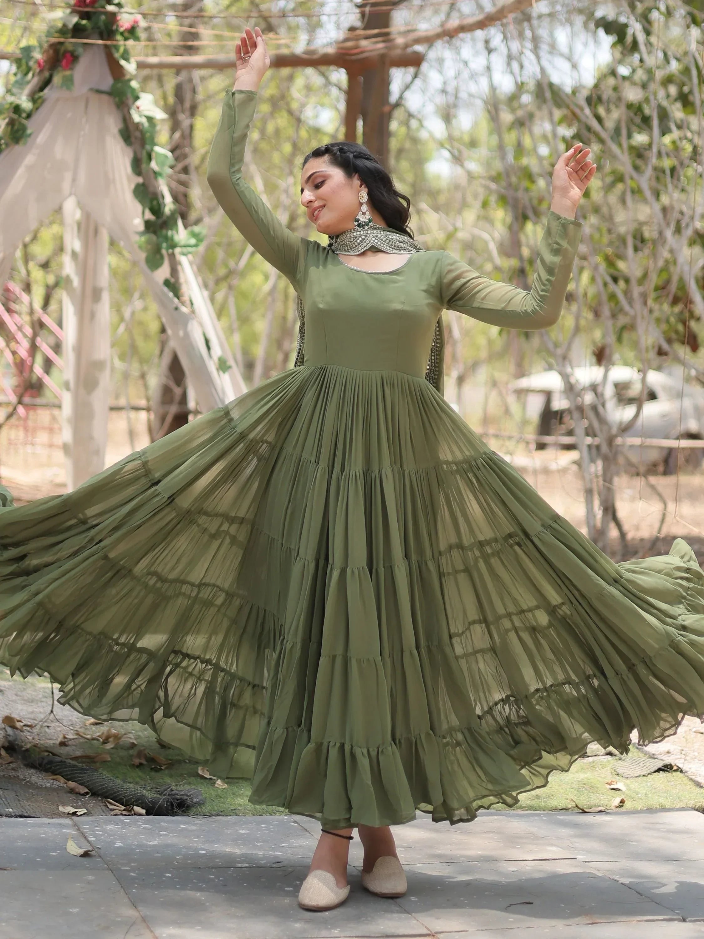 Woman in flowy olive green Anarkali gown with dupatta, outdoor setting, Indian ethnic wear