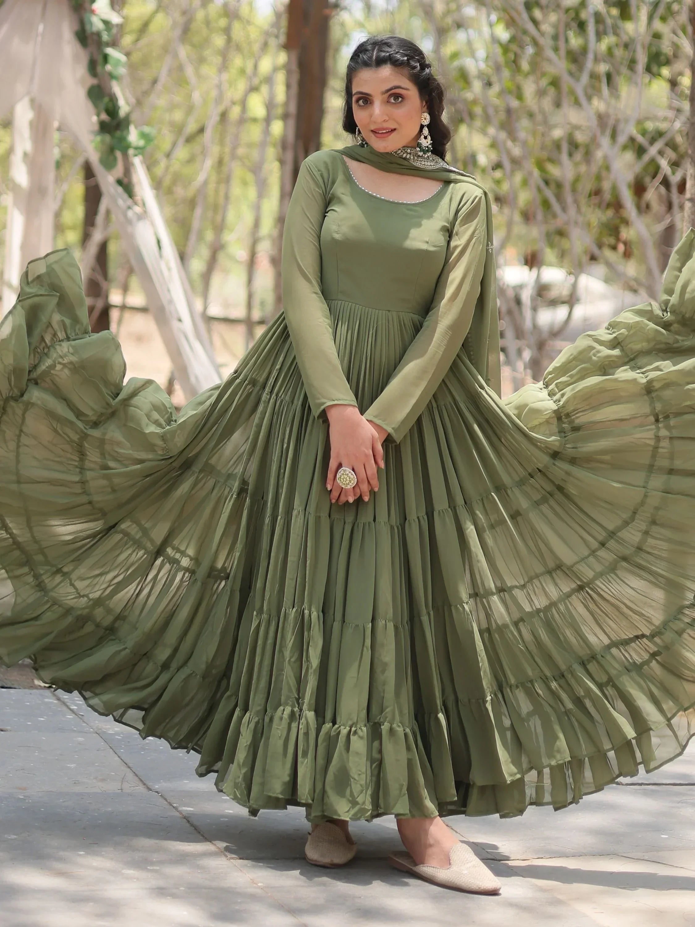 Woman in olive green Anarkali dress with dupatta, ruffled hem, and statement jewelry outdoors