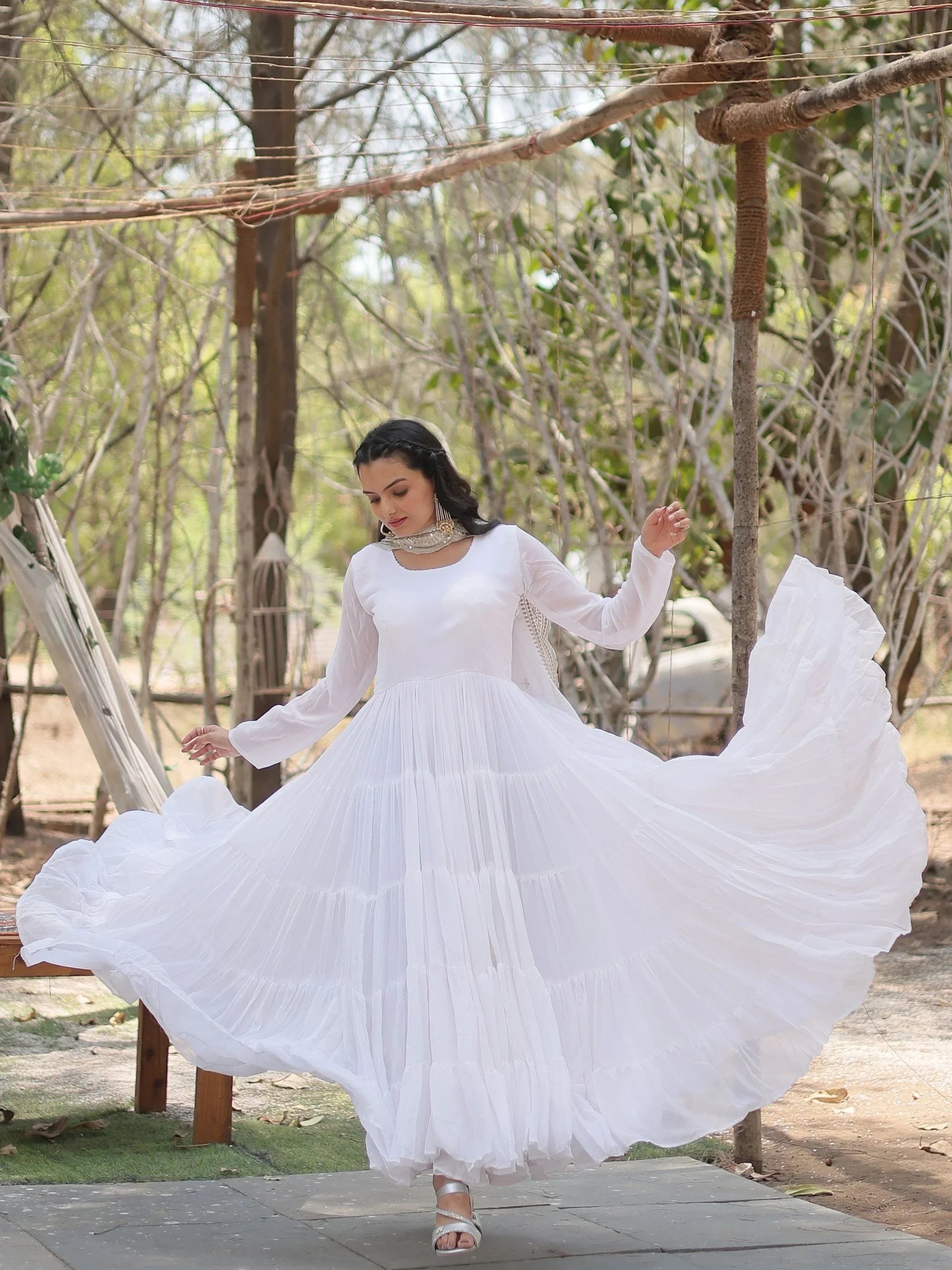 Woman in a flowing white ethnic gown with long sleeves, posing outdoors in natural light