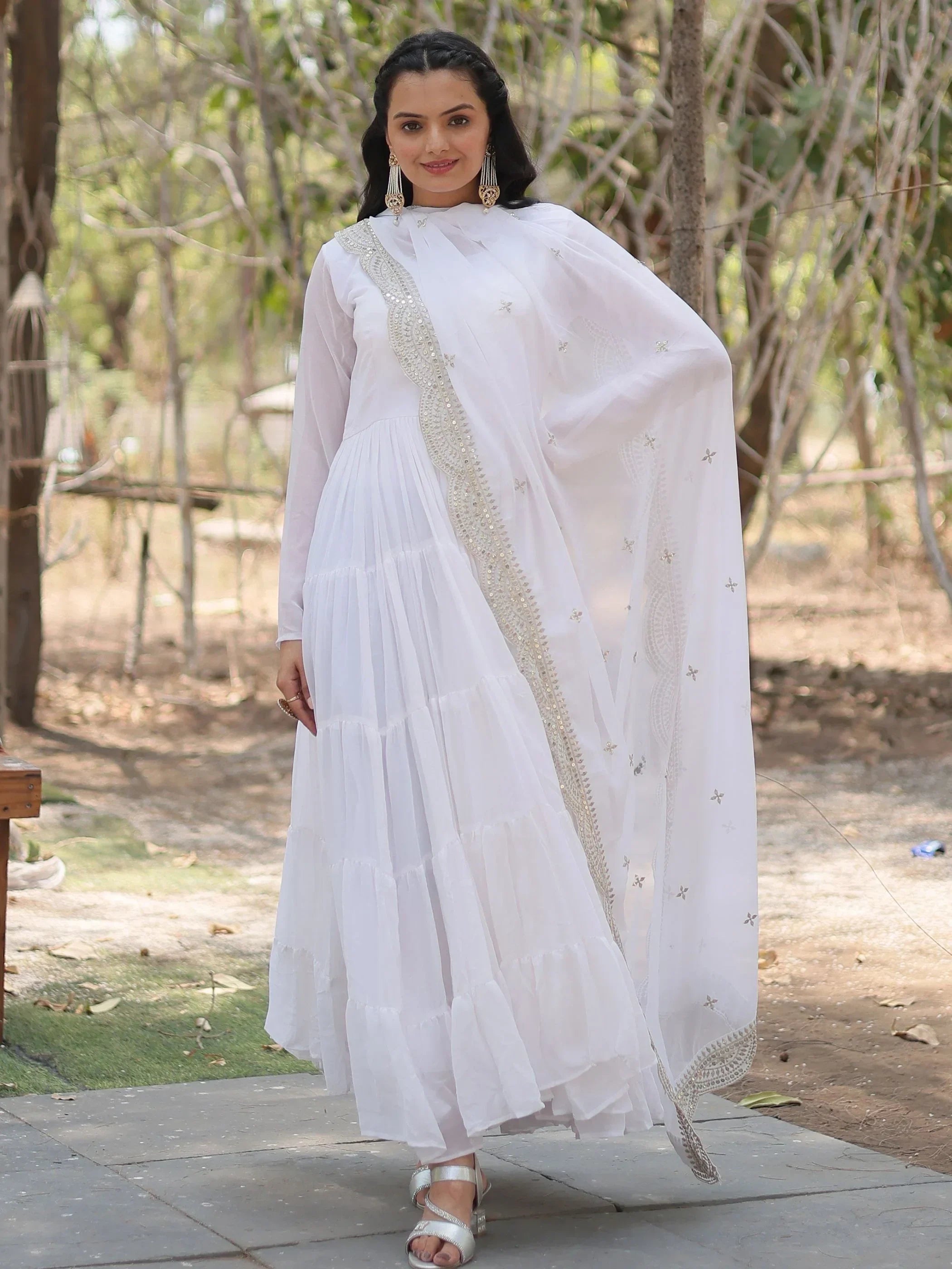 Woman wearing an elegant white Anarkali suit with dupatta and silver embroidery outdoors