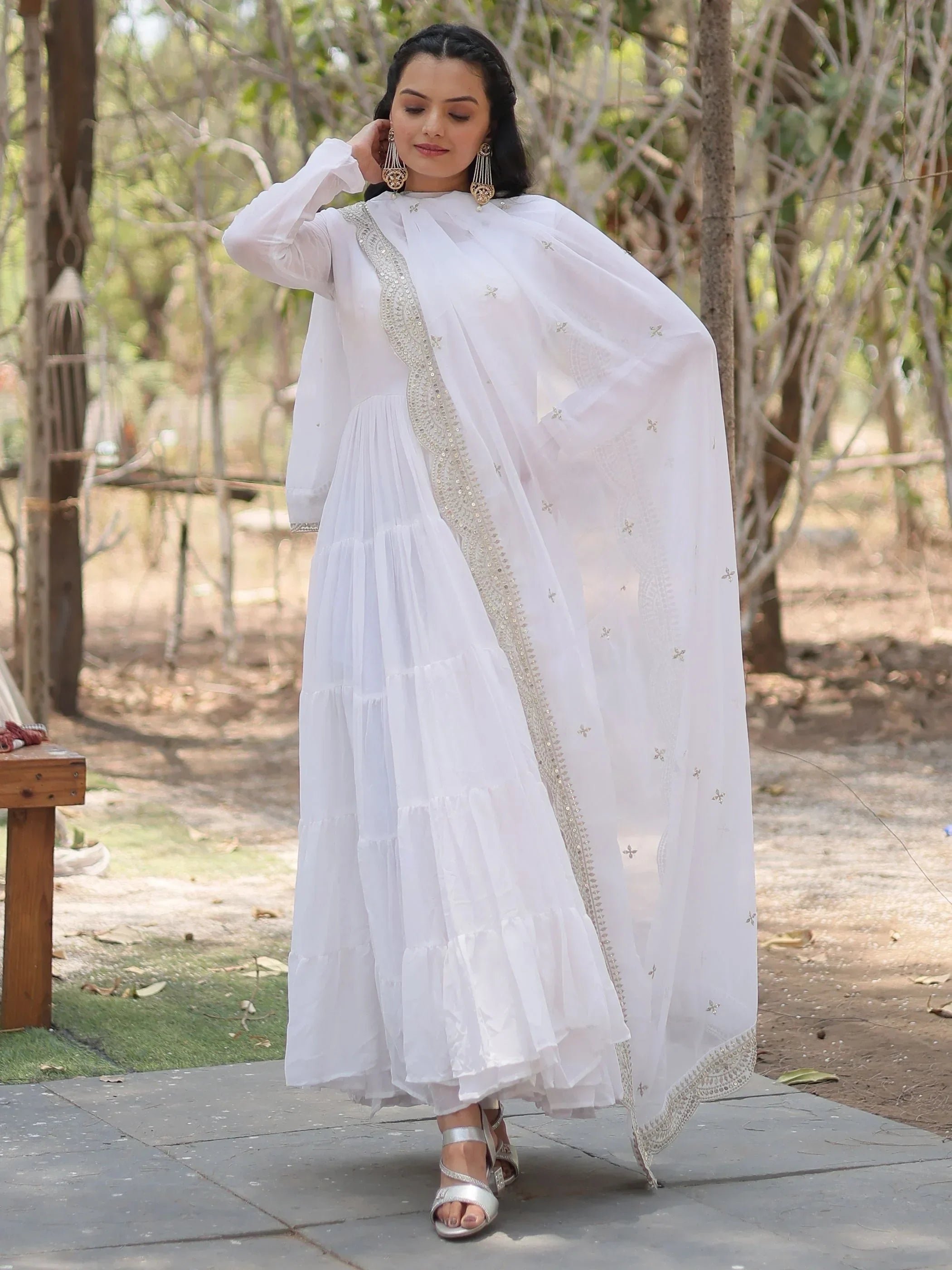 Woman wearing white embroidered Indian Anarkali suit with dupatta, outdoor setting