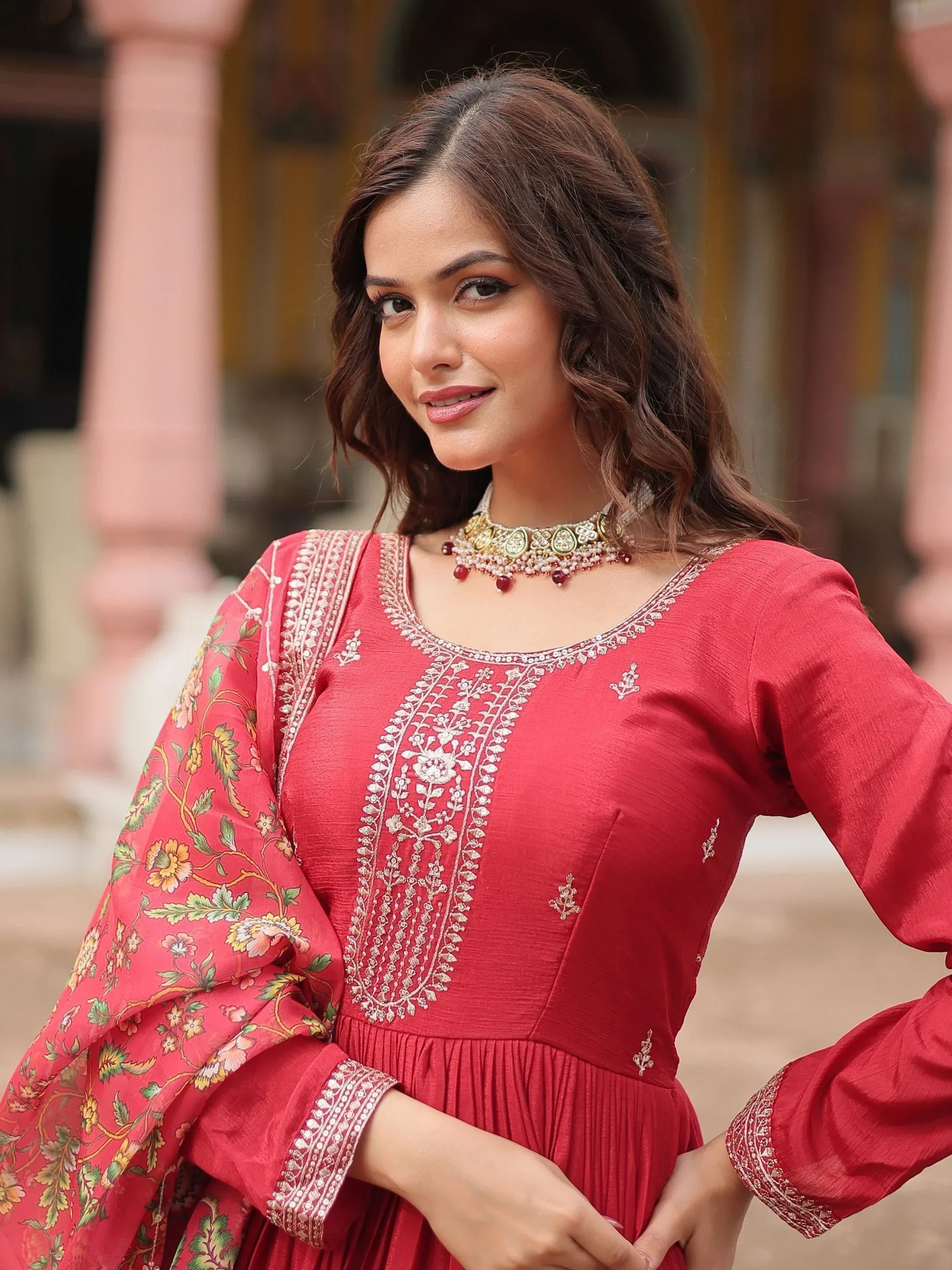 Woman in maroon ethnic gown with floral embroidered dupatta, traditional jewelry, outdoor setting