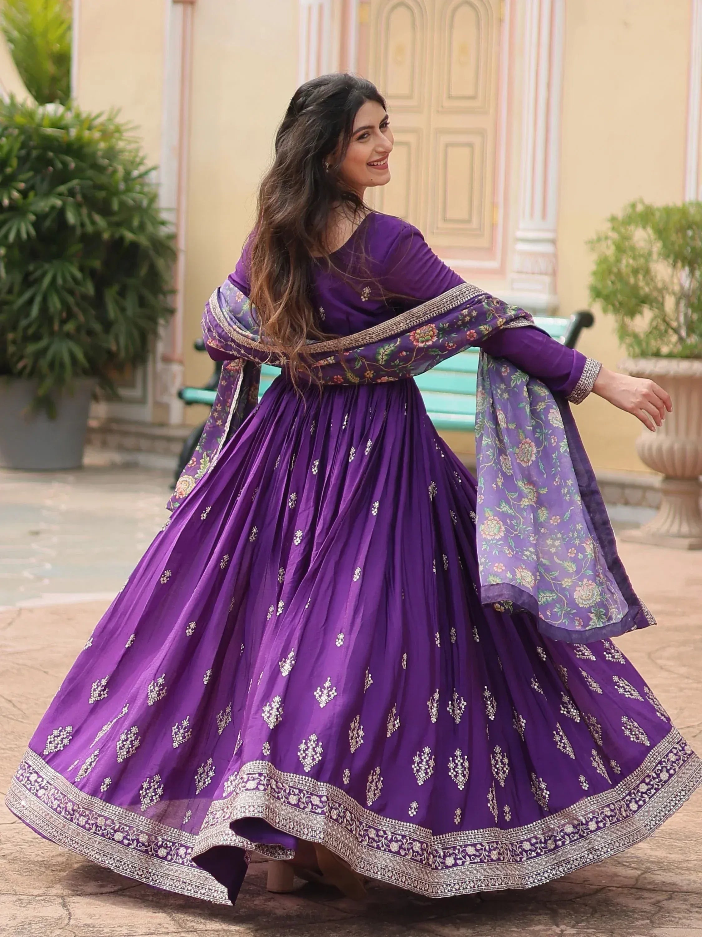 Woman twirling in purple embroidered Indian ethnic gown with floral dupatta outdoors