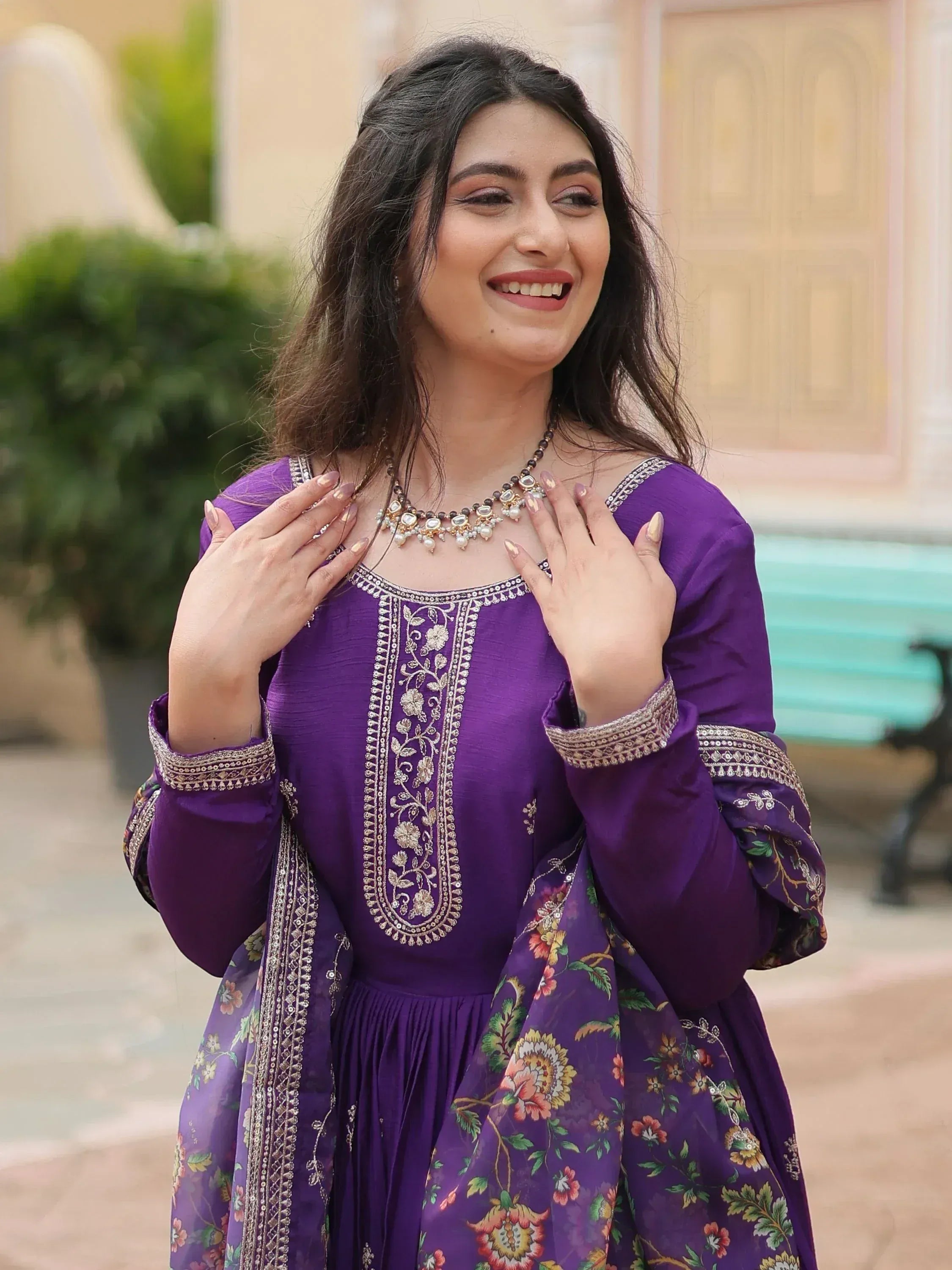 Woman in purple embroidered ethnic gown with floral dupatta, smiling outdoors