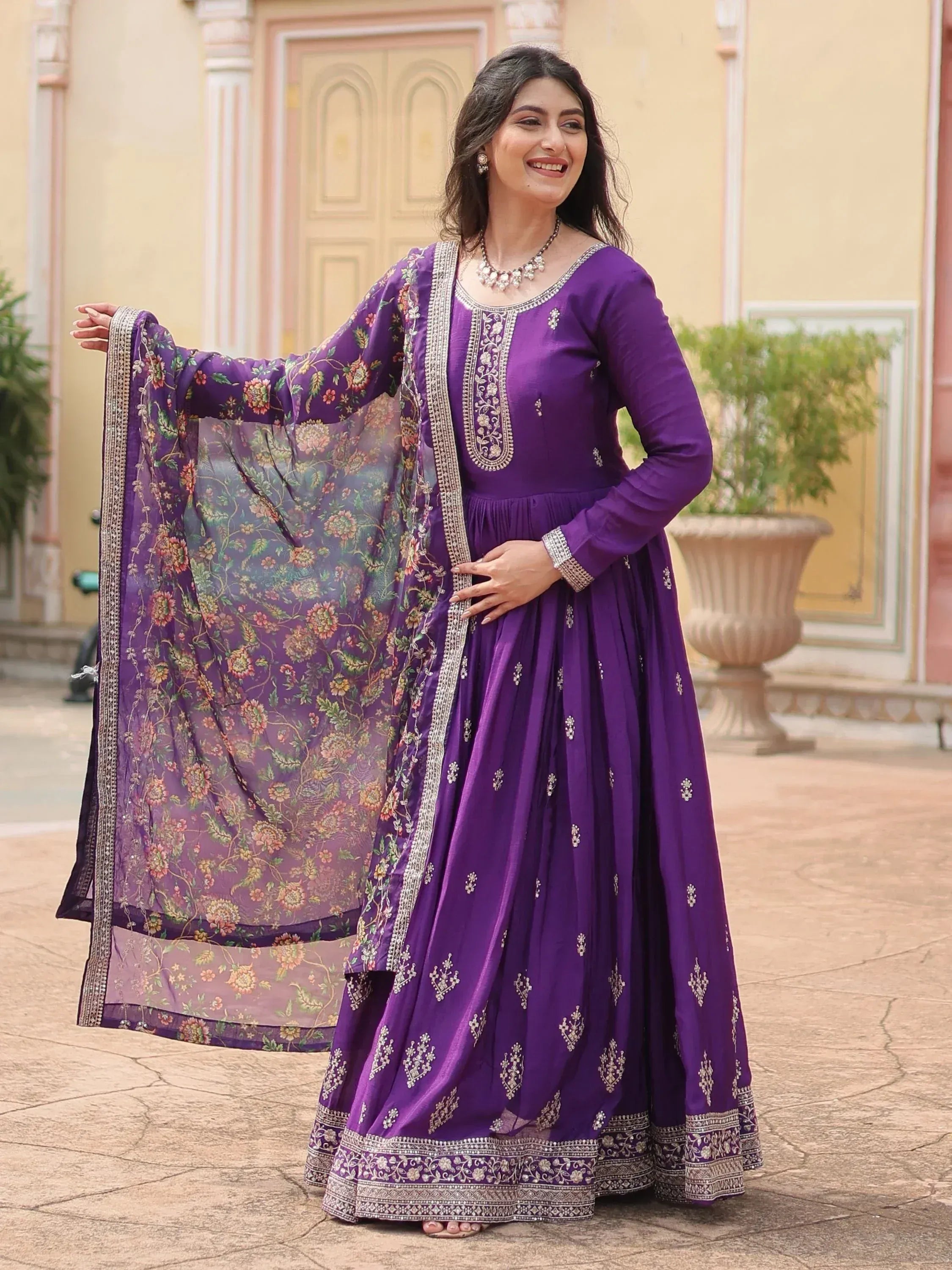 Woman wearing a purple embroidered ethnic gown with floral dupatta, outdoor setting