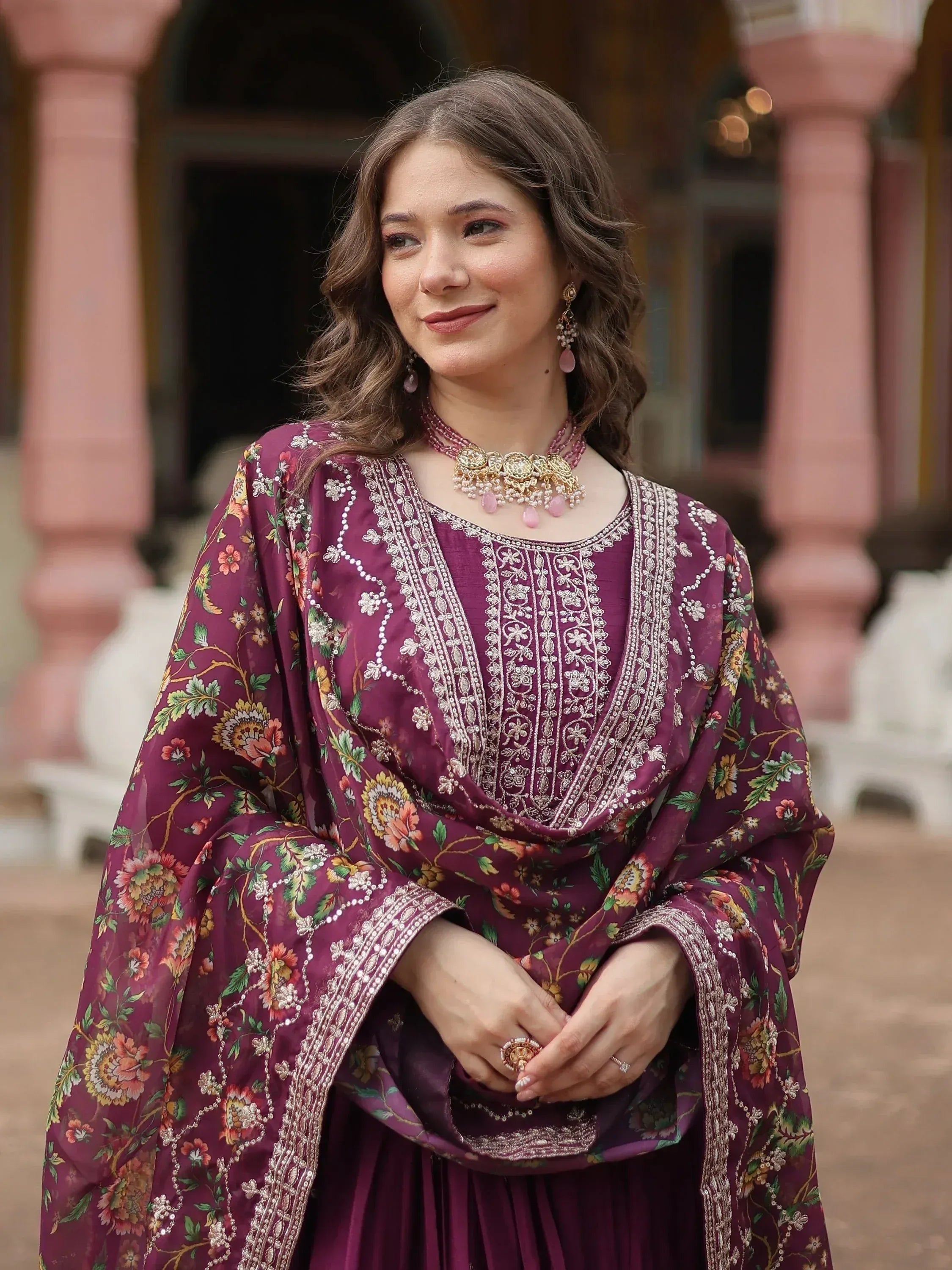 Woman in wine-colored embroidered salwar kameez with floral dupatta and statement jewelry