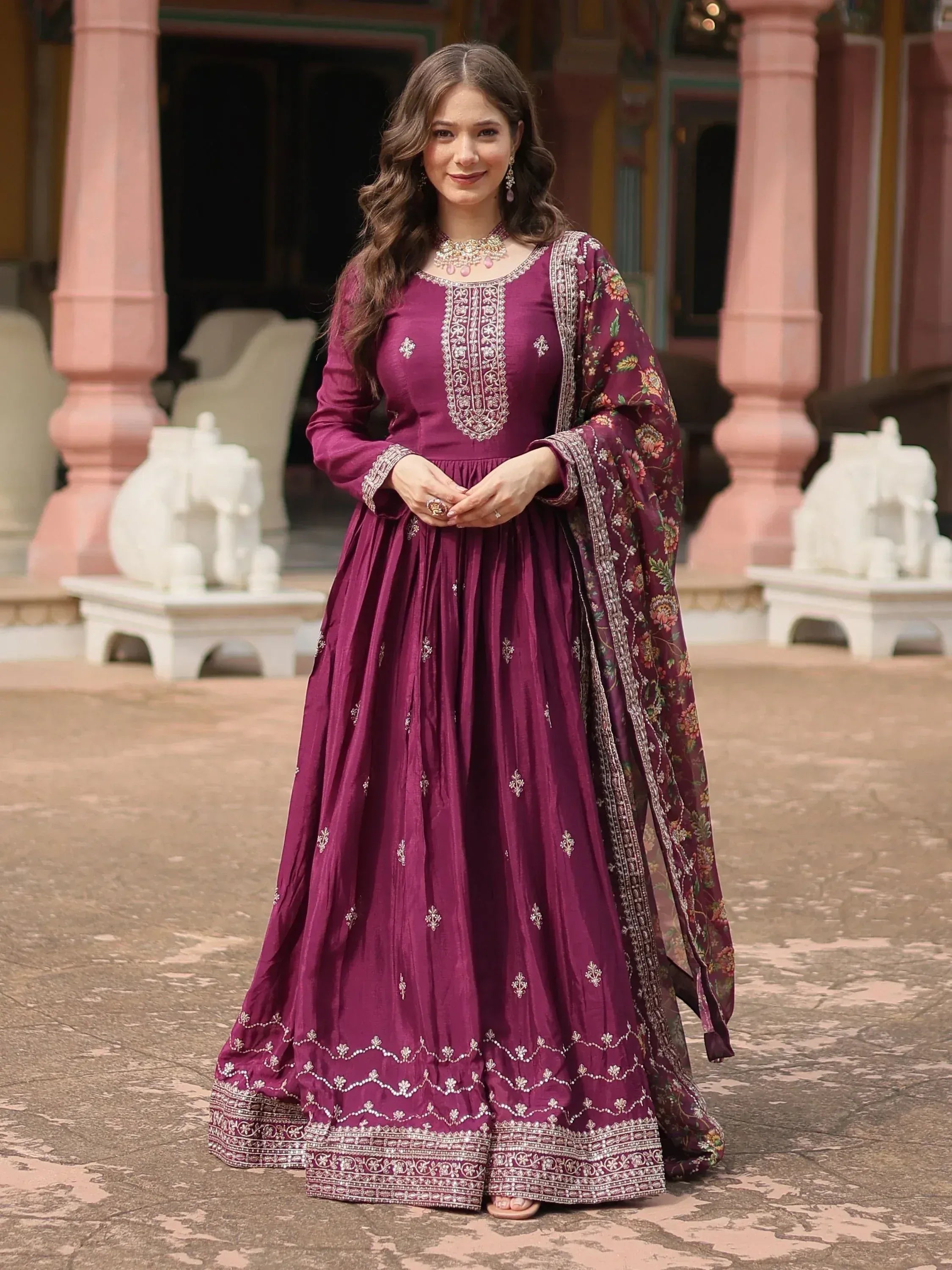 Woman in wine-colored embroidered Anarkali suit with matching floral dupatta, outdoor setting