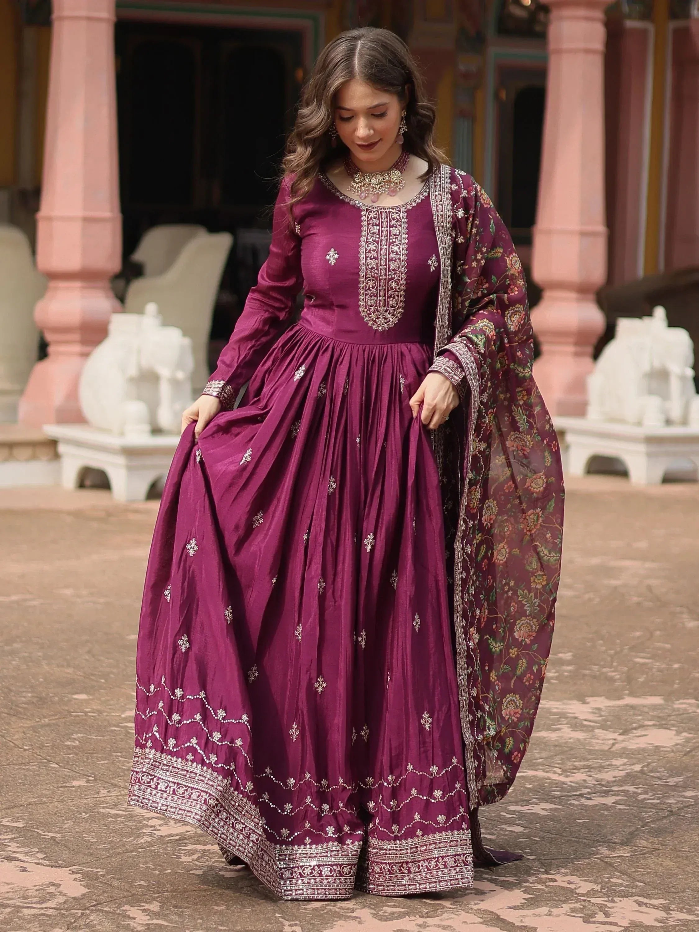 Woman wearing wine-colored embroidered Anarkali gown with floral dupatta, ethnic jewelry