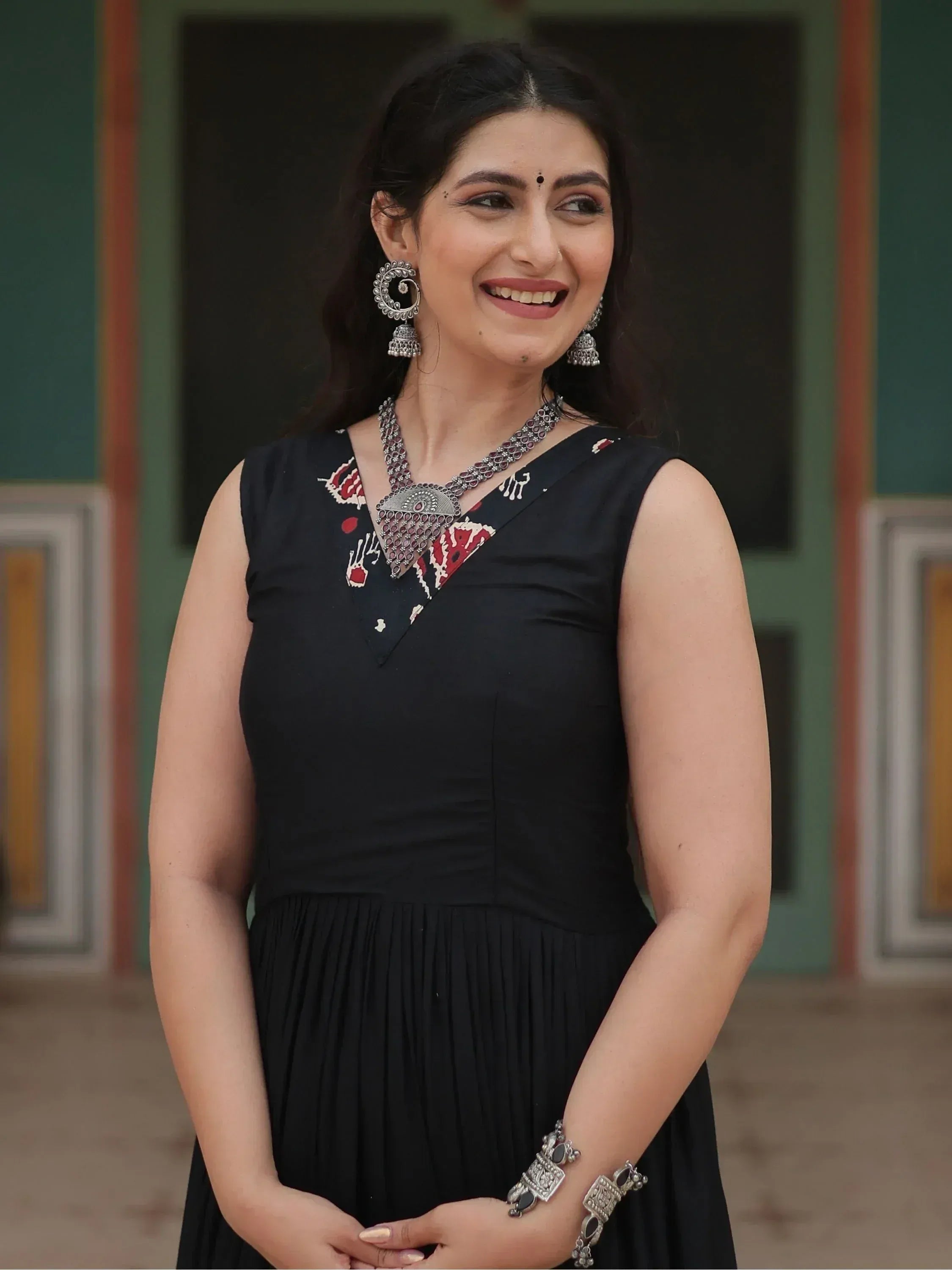 Woman in black ethnic gown with red white print, silver jewelry, smiling outdoors