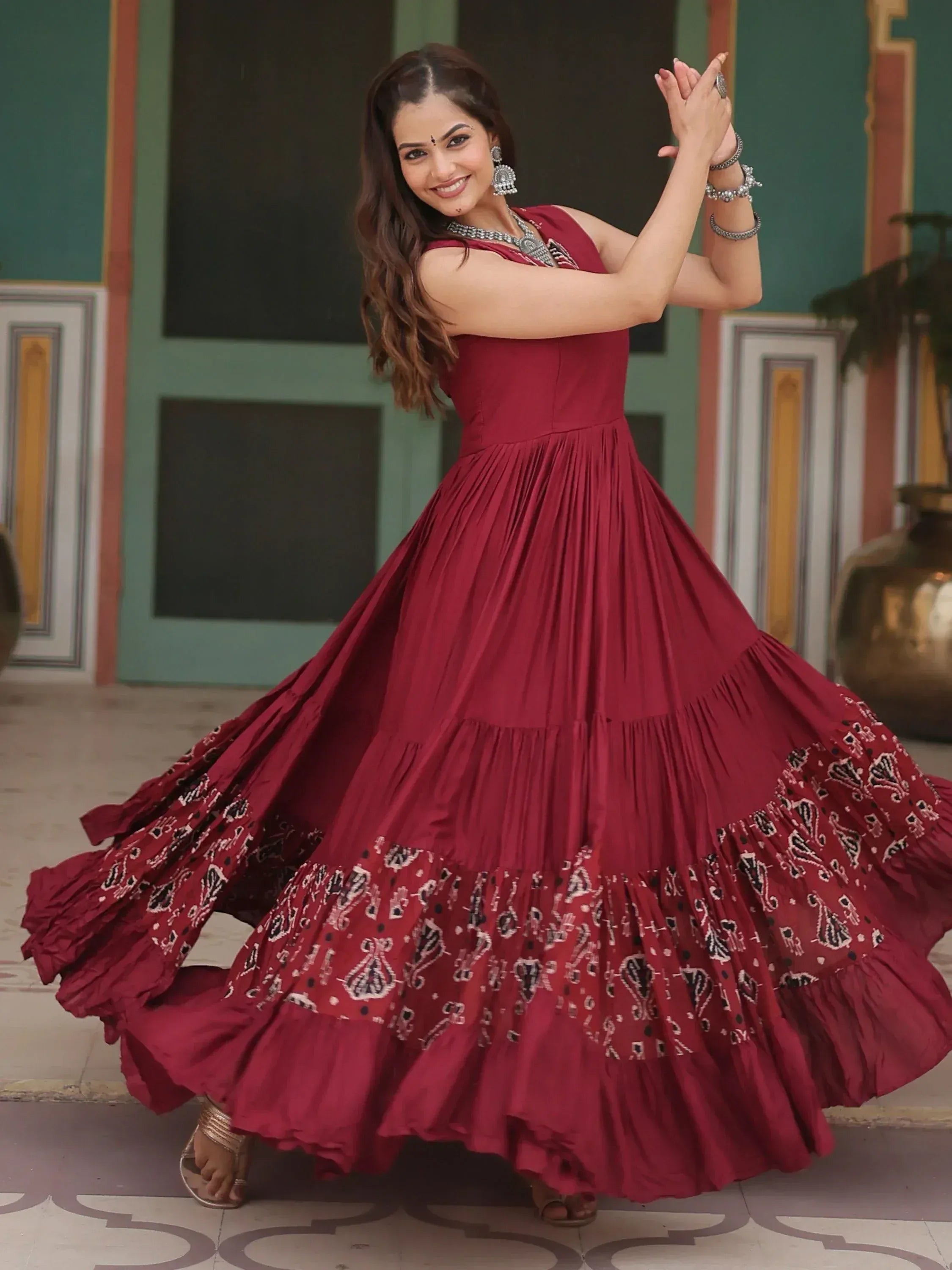Woman in maroon ethnic gown with printed tiered skirt, perfect for Indian occasions and festive wear.
