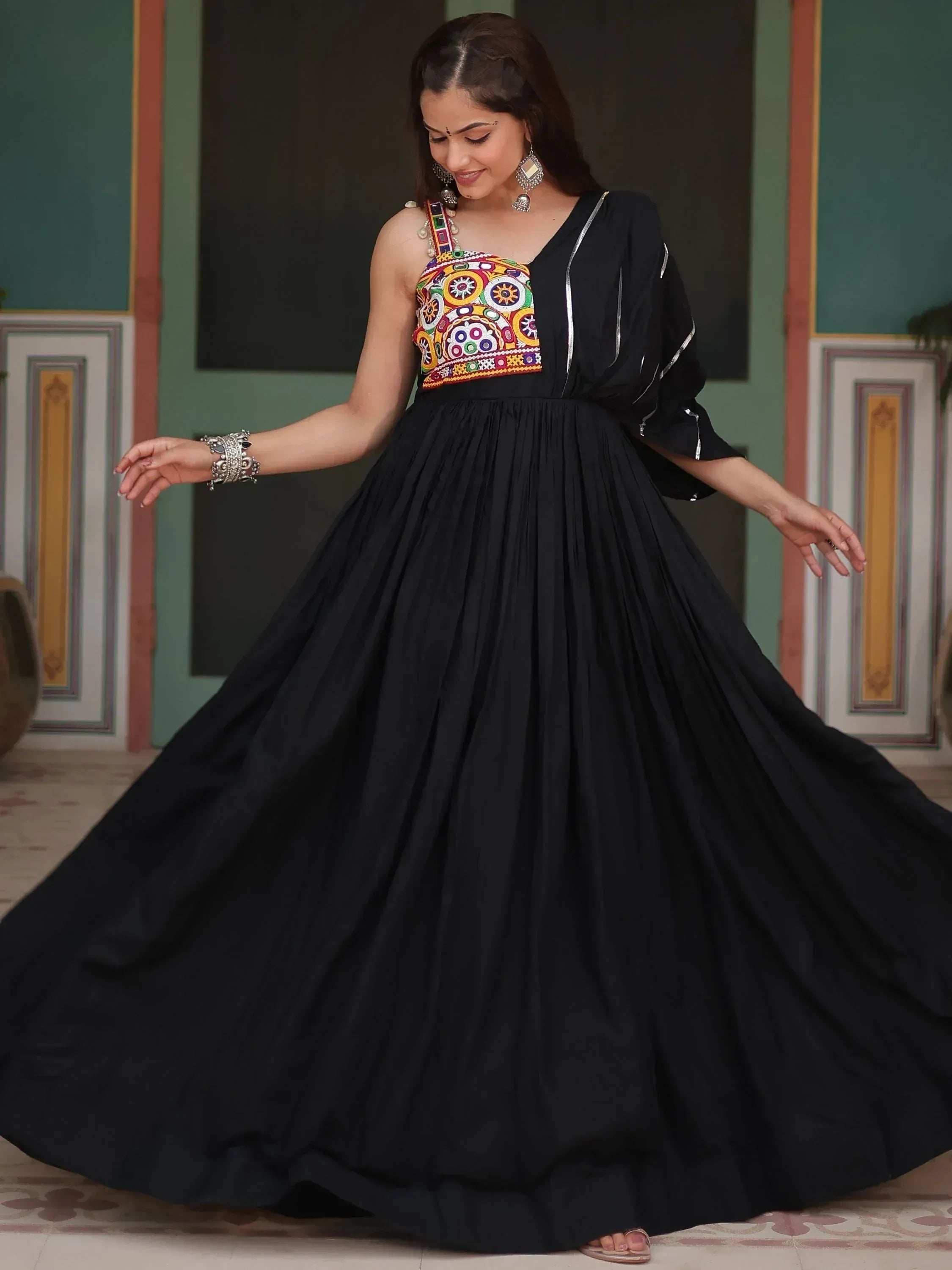 Woman in a black ethnic gown with a colorful embroidered bodice, traditional jewelry, and flared skirt