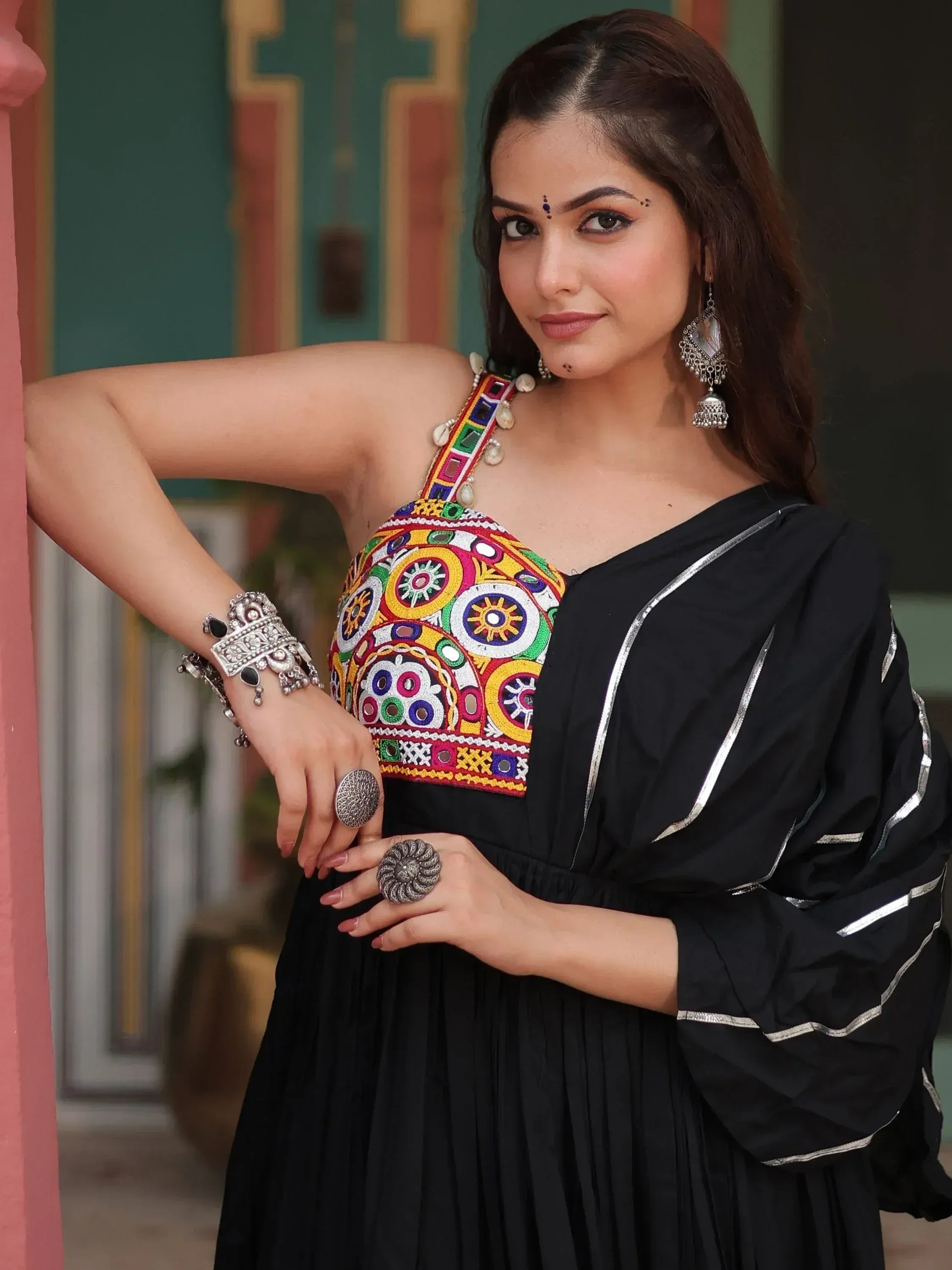 Woman in black ethnic gown with colorful embroidered blouse, wearing silver jewelry